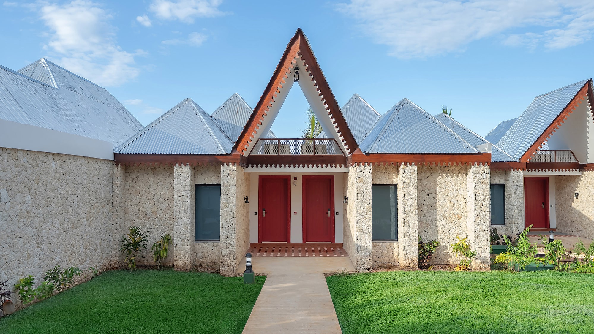 Stone tropical resort villas with peaked metal roofs, red doors, green lawn.