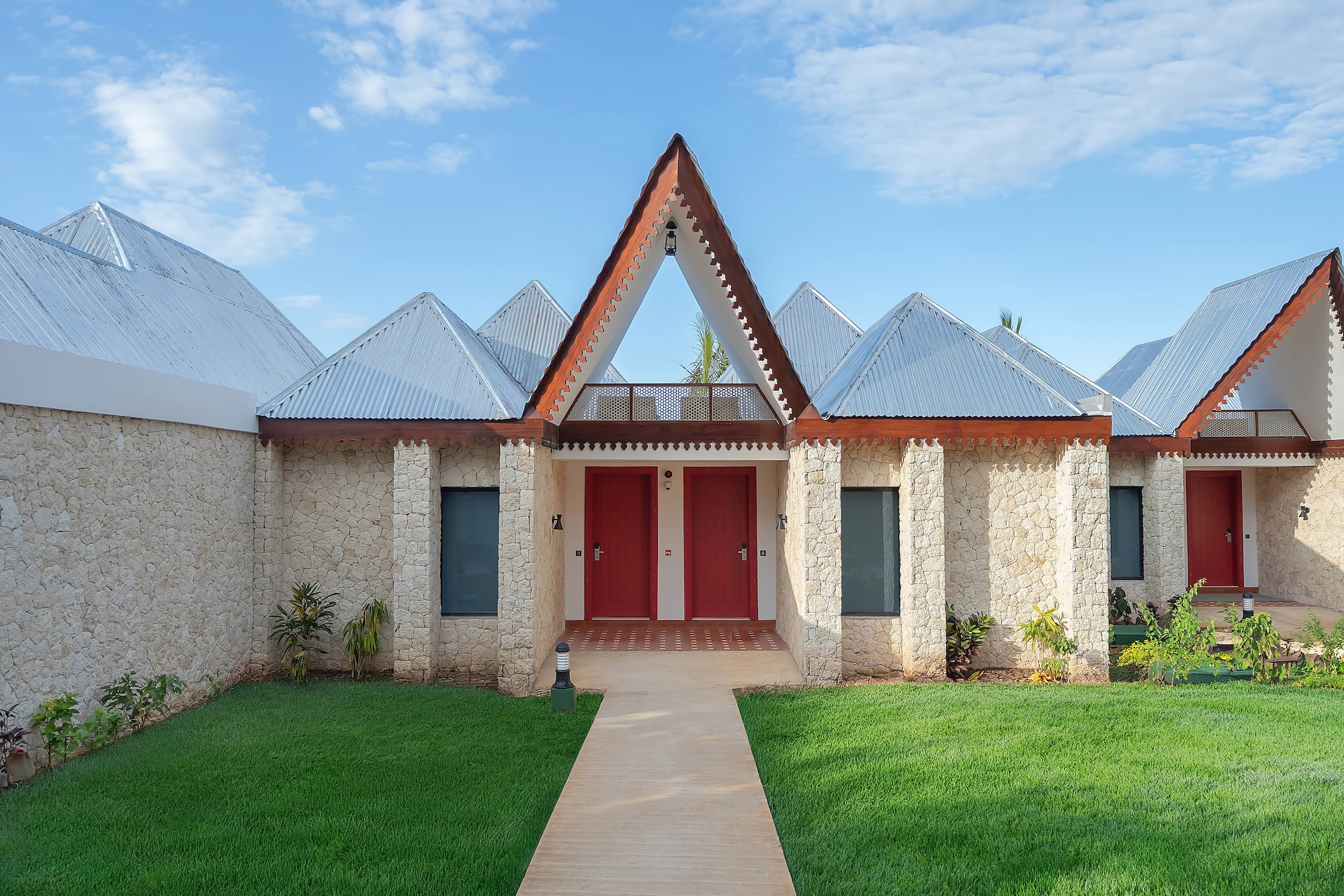 Stone tropical resort villas with peaked metal roofs, red doors, green lawn.