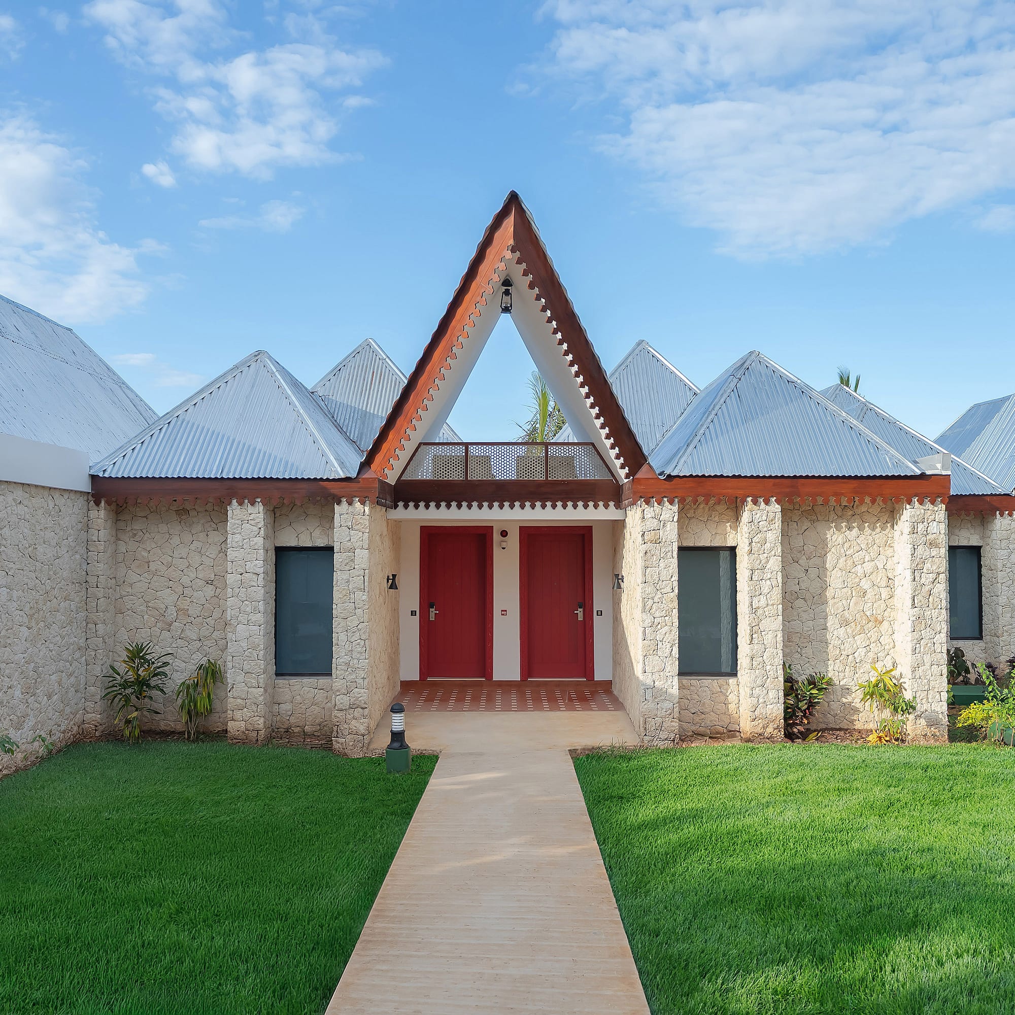 Stone tropical resort villas with peaked metal roofs, red doors, green lawn.