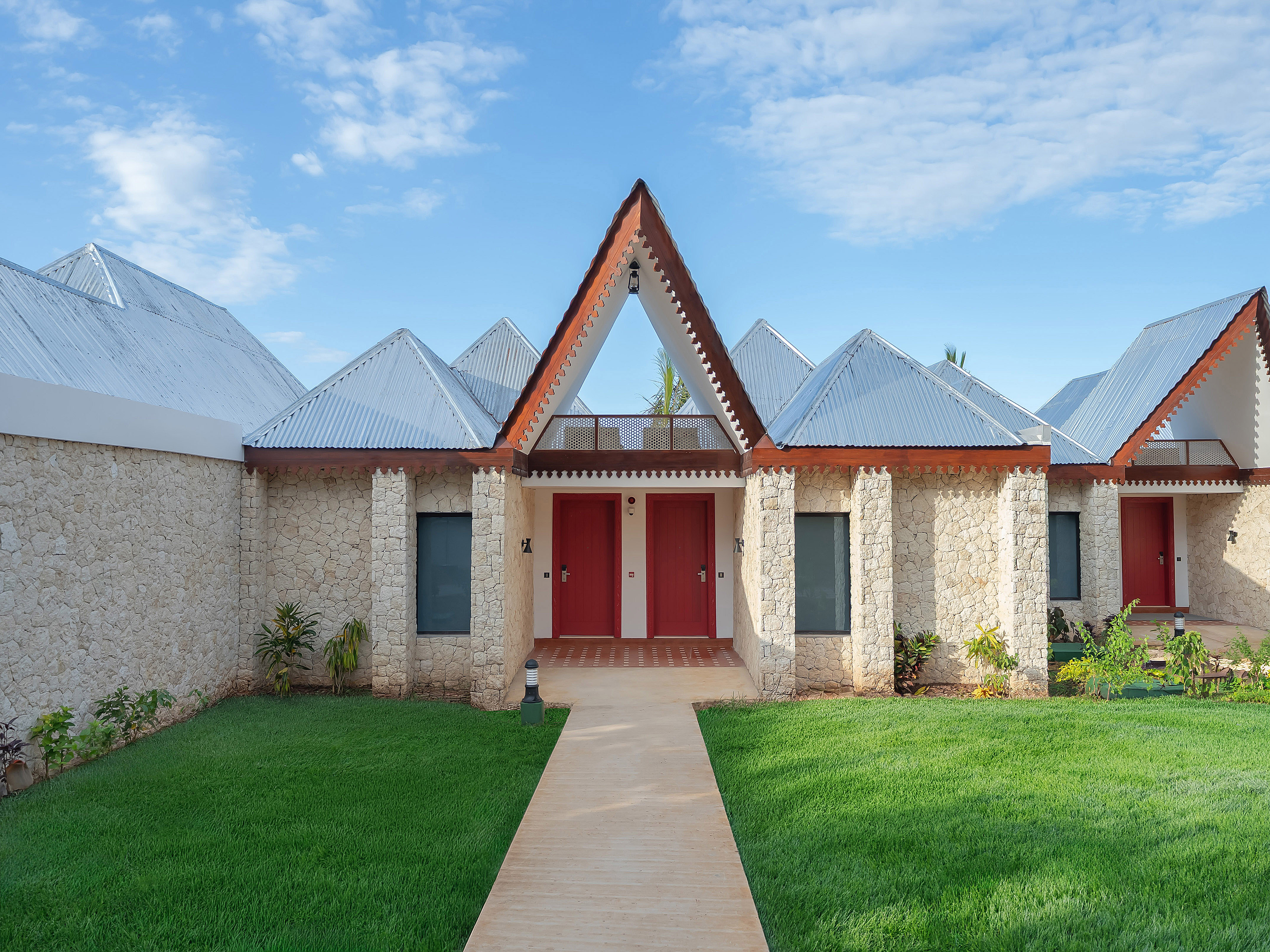 Stone tropical resort villas with peaked metal roofs, red doors, green lawn.