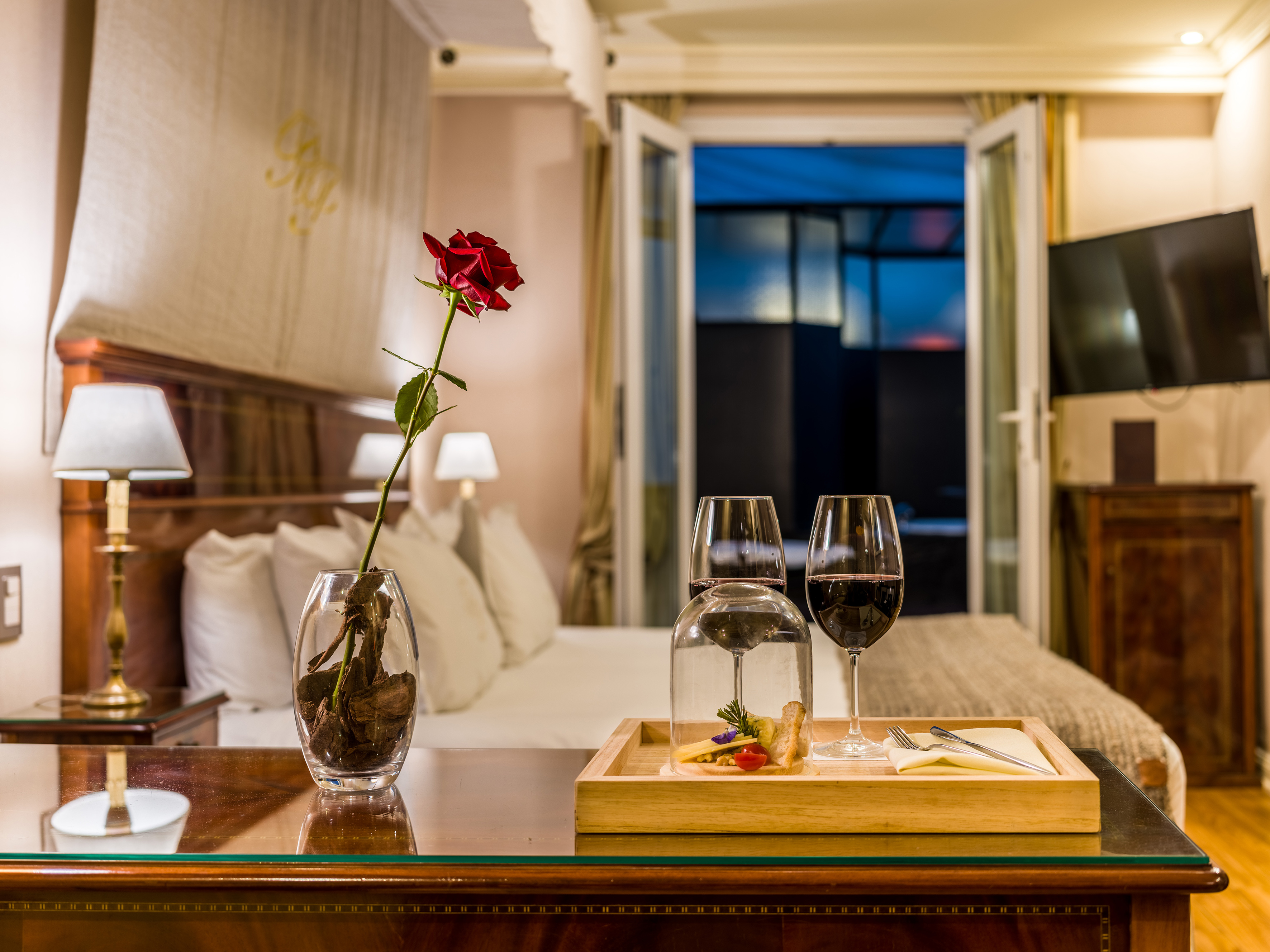 Elegant hotel room with red rose, wine glasses, and a cheese platter.