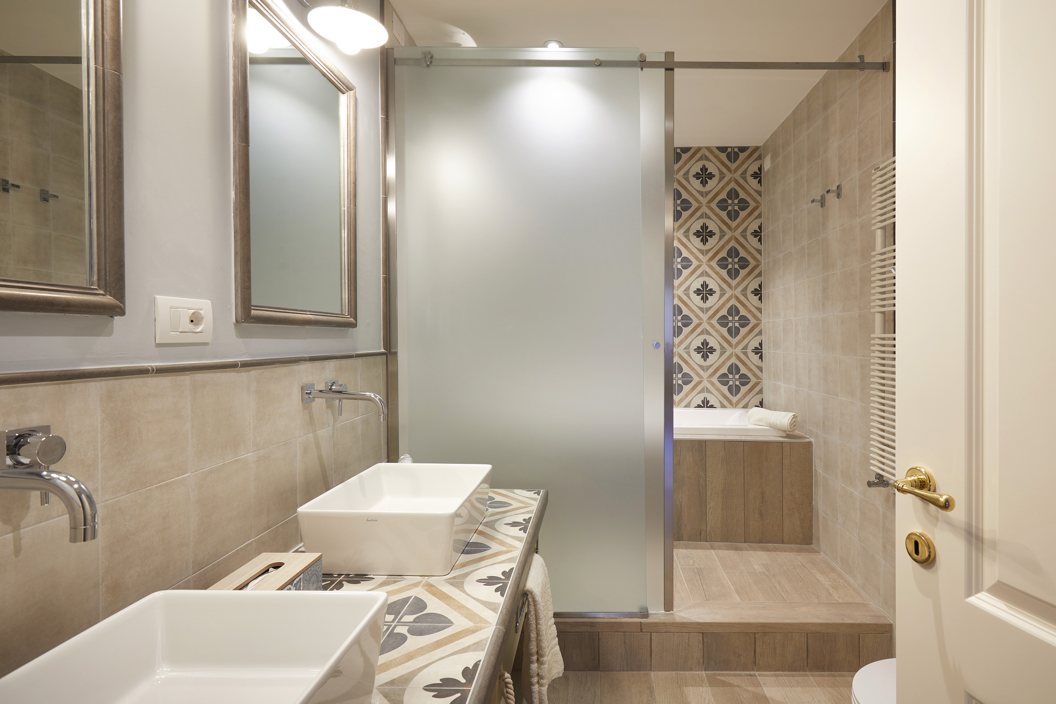 Modern bathroom with double vanity, frosted glass, bathtub, and patterned tiles.
