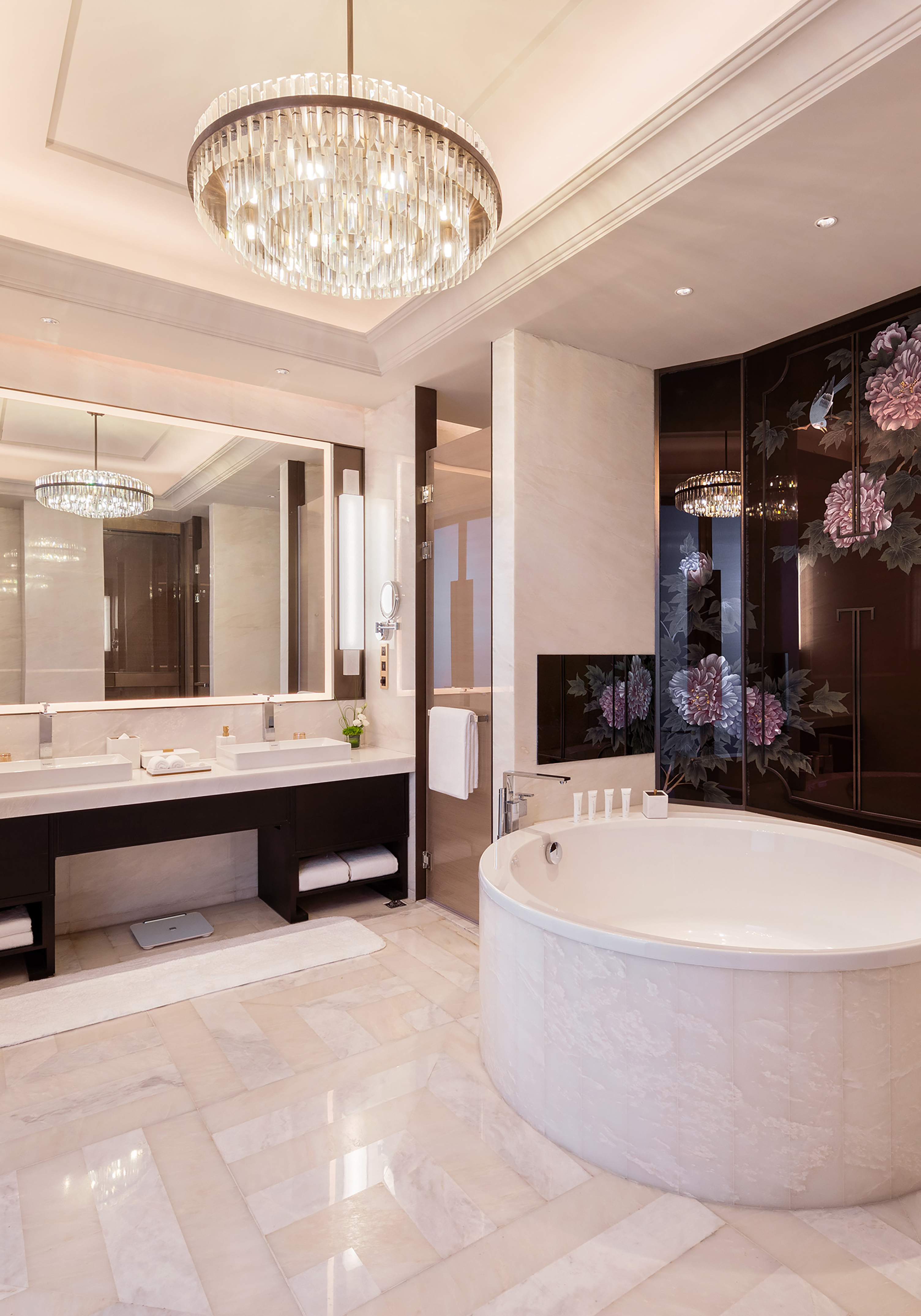 Luxury bathroom: crystal chandelier, double vanity, oval tub, floral art.