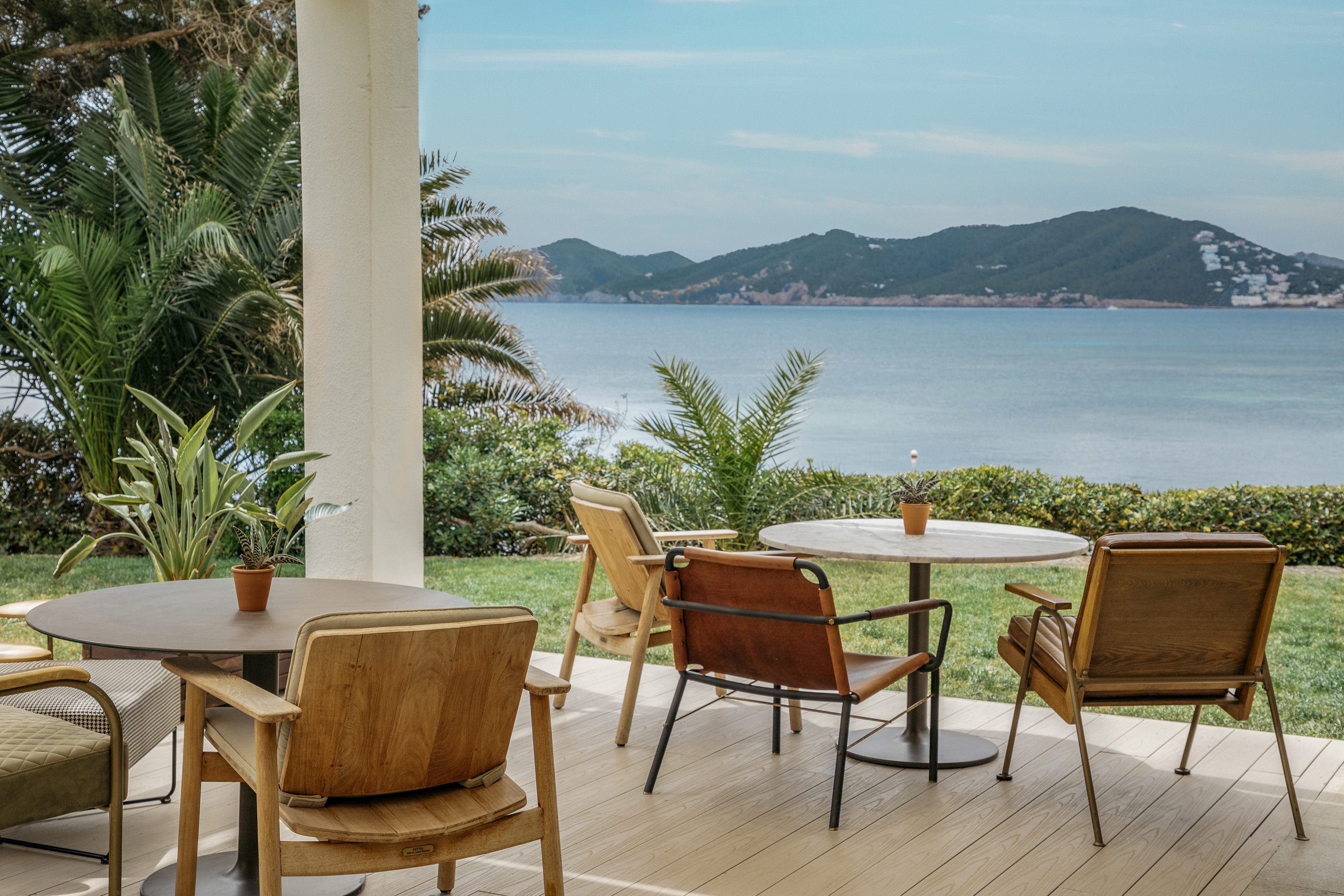 Coastal terrace with modern outdoor seating, palm trees, and scenic sea view.
