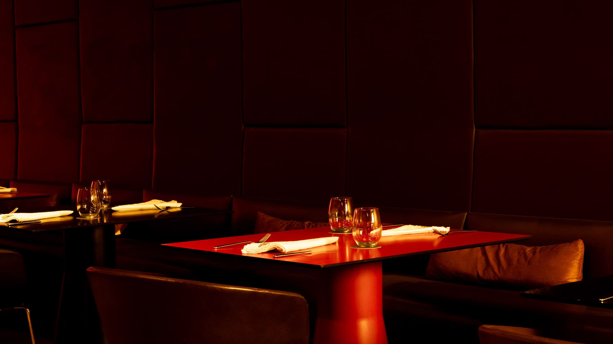 Modern restaurant interior with red table, pendant lighting, and dark wood floor.