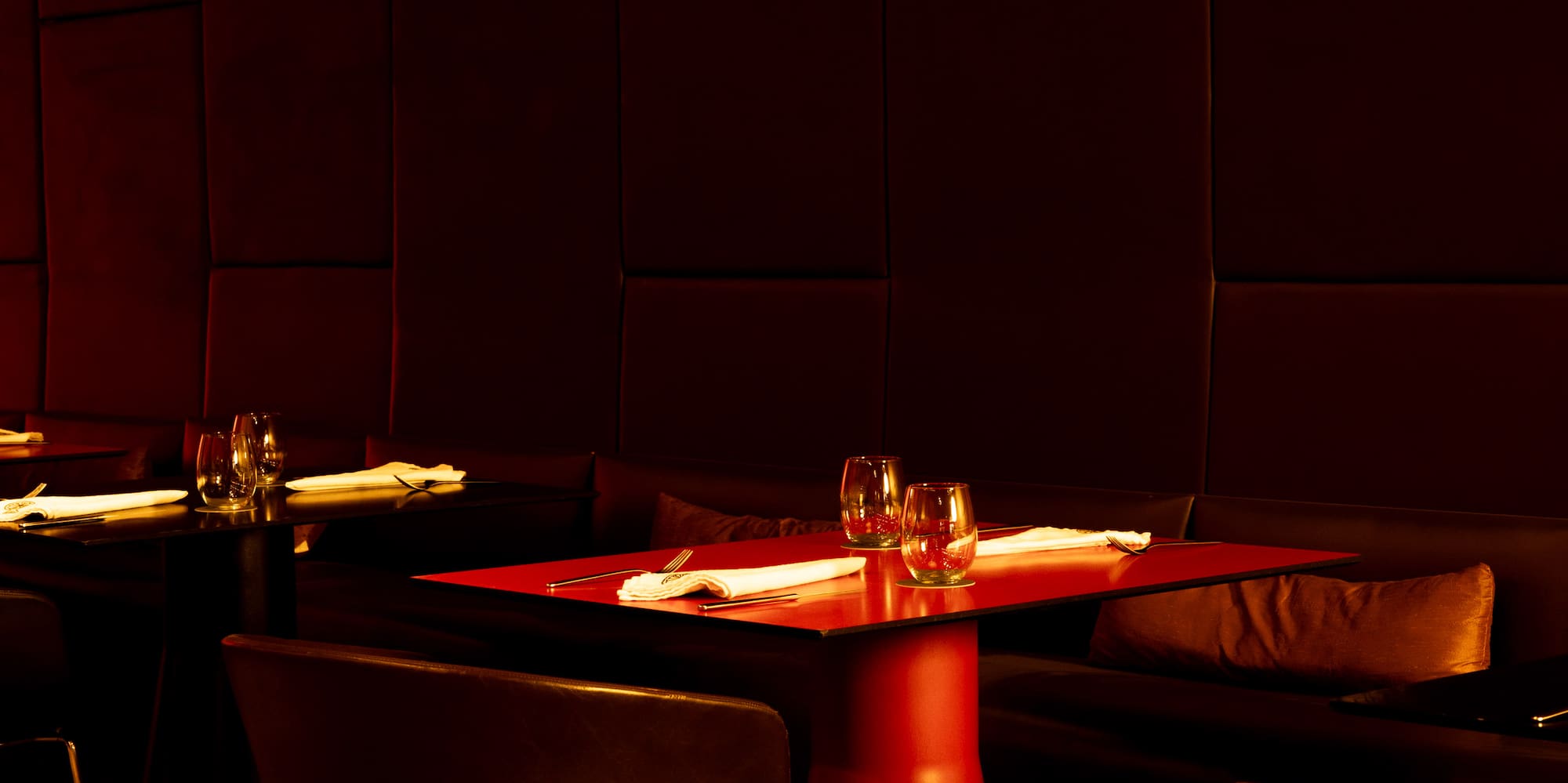 Modern restaurant interior with red table, pendant lighting, and dark wood floor.