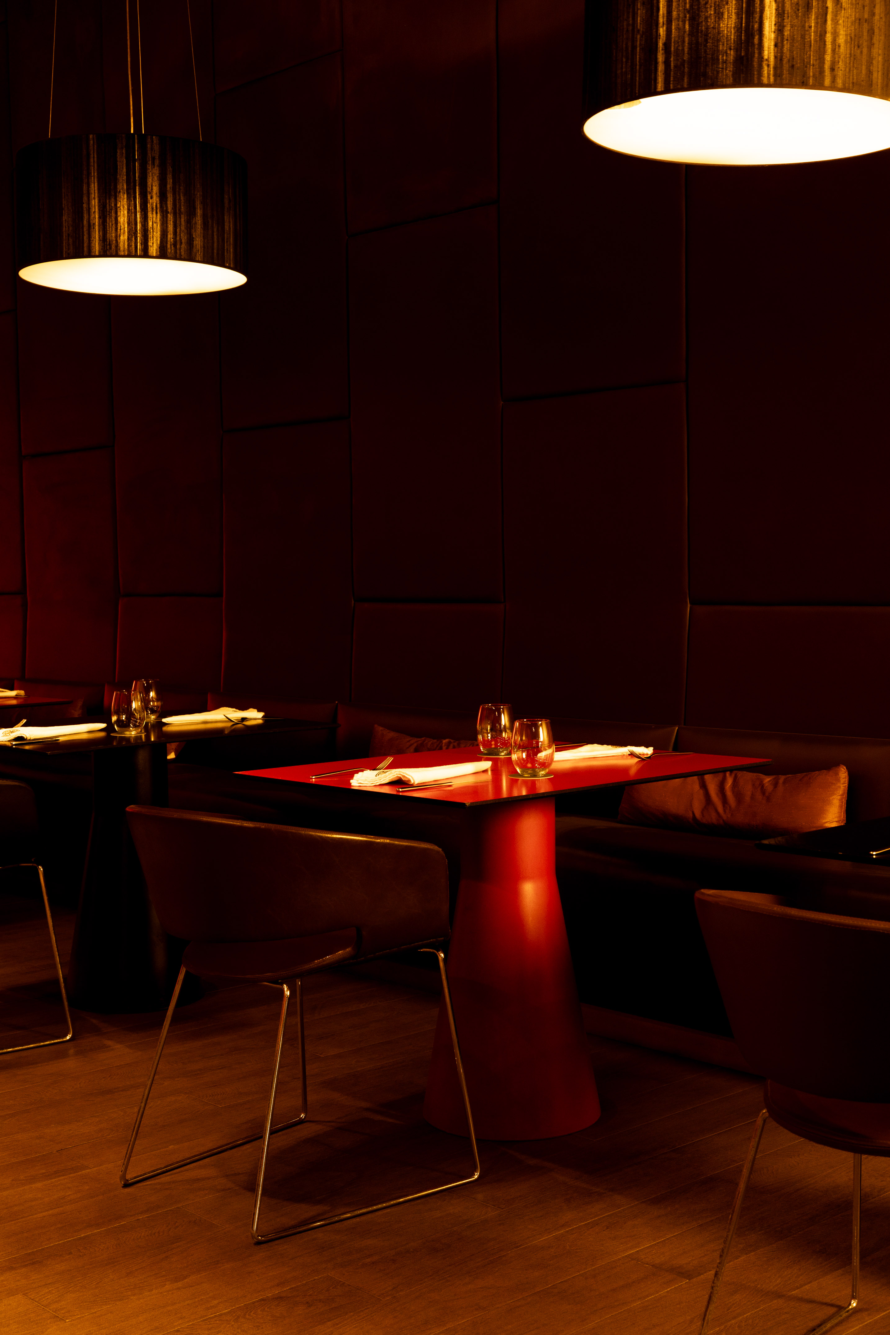 Modern restaurant interior with red table, pendant lighting, and dark wood floor.