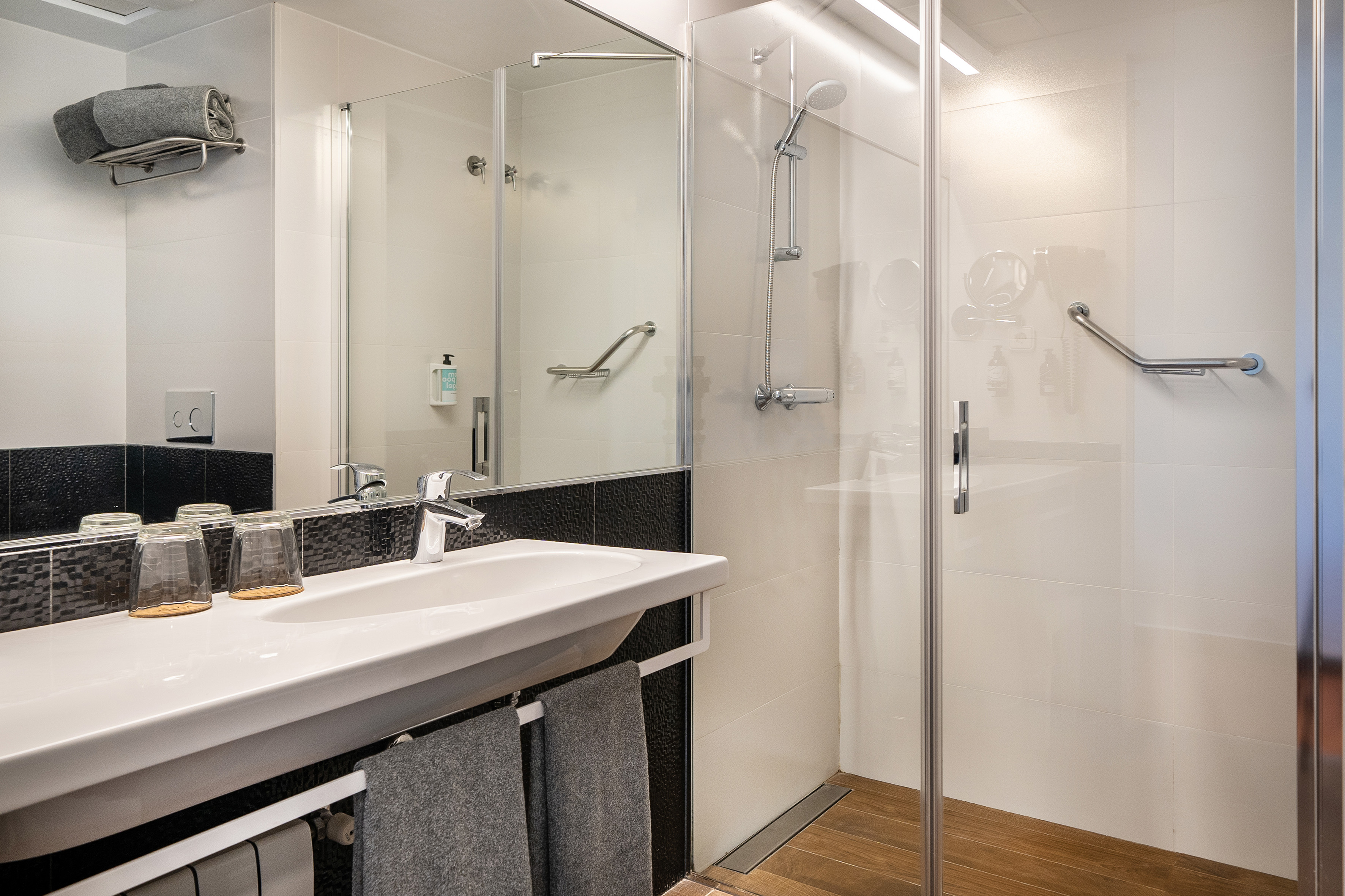Modern bathroom with white sink, glass shower, accessible grab bar, and wood floor.
