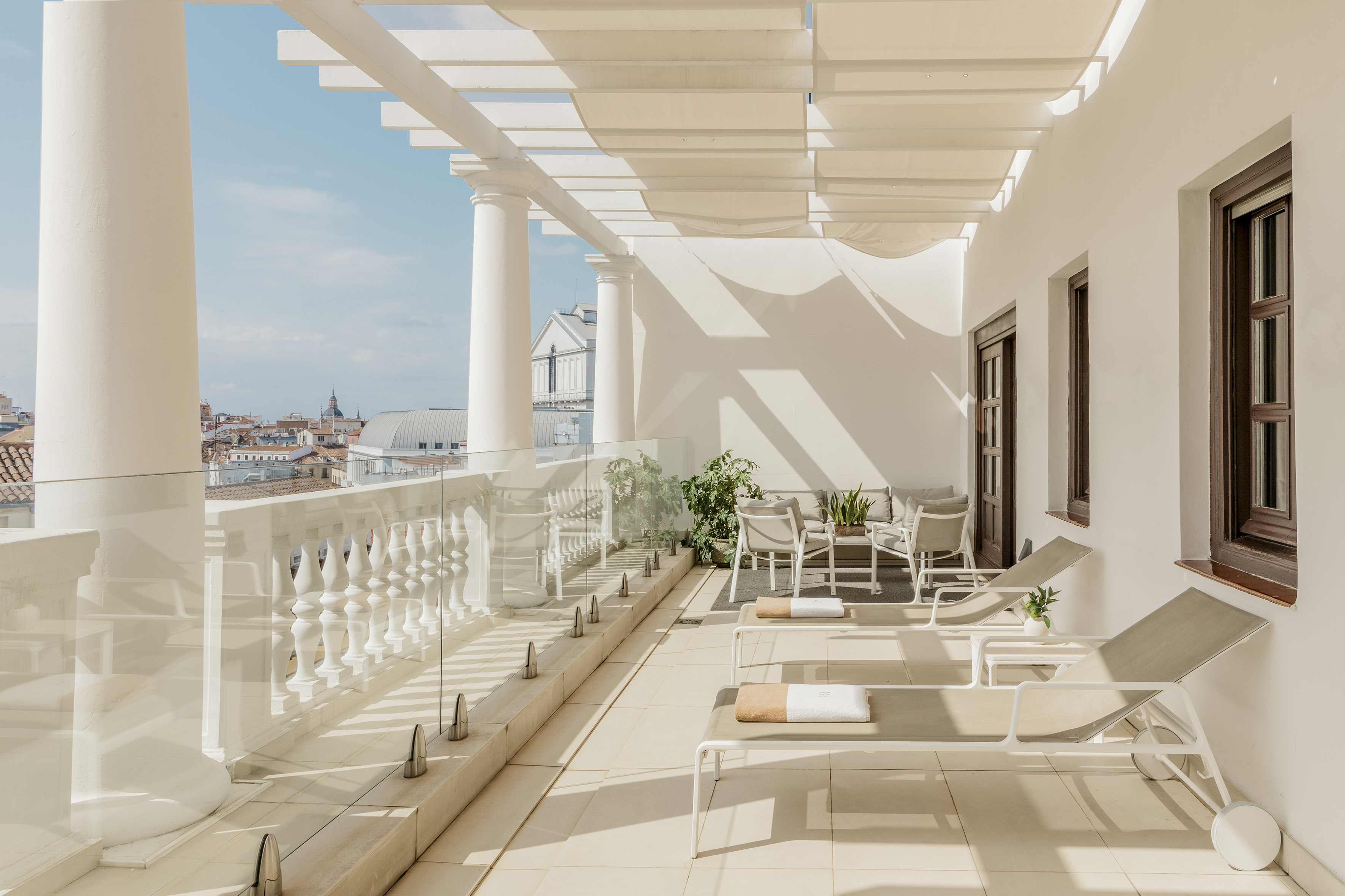 Luxurious rooftop terrace with sun loungers, pergola, and city view.