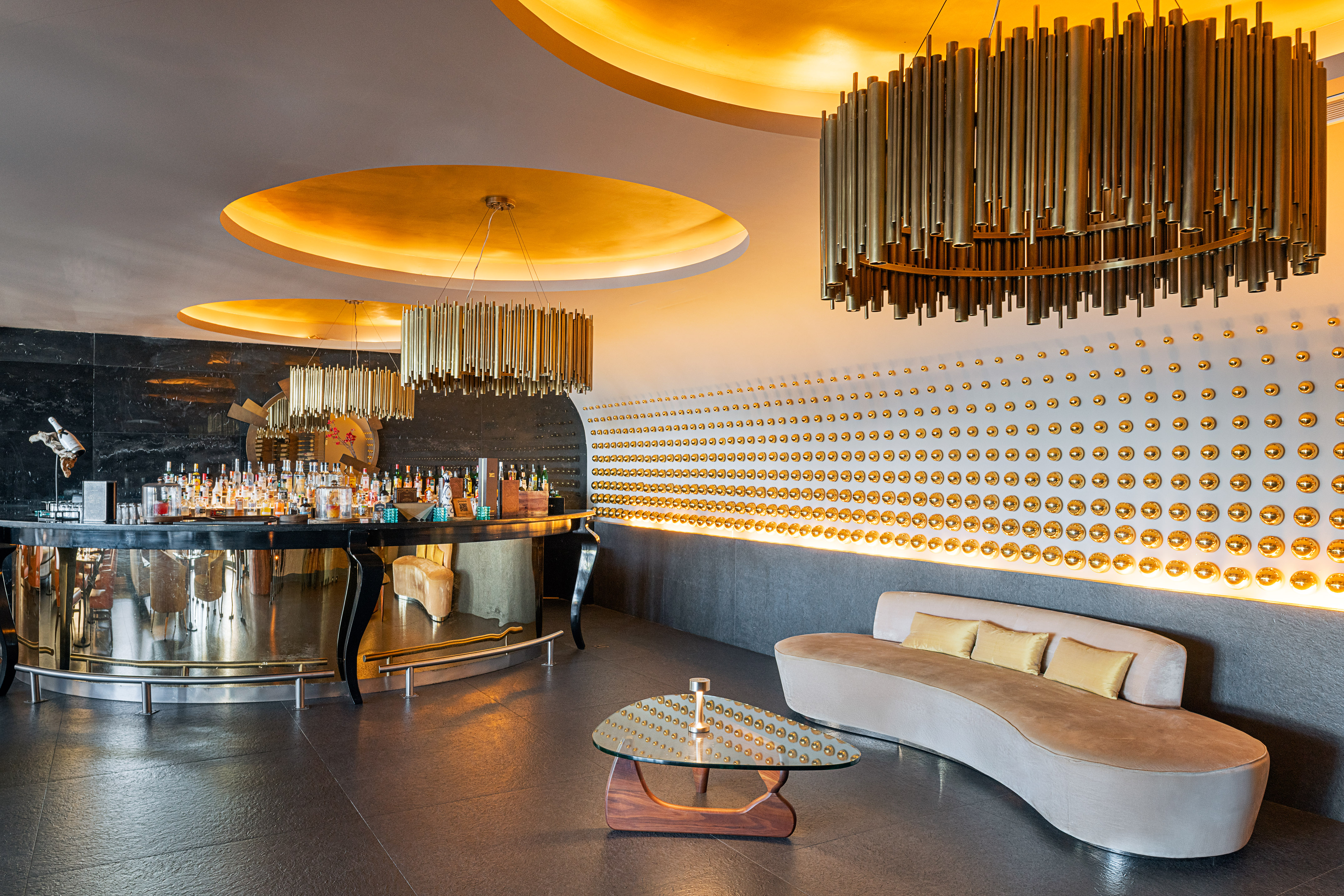 Elegant hotel bar featuring golden chandeliers, a studded wall, and modern seating.