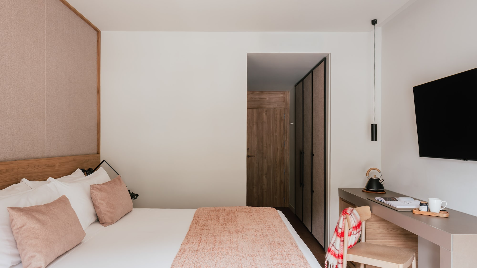 Modern hotel bedroom with cozy bed, wood headboard, desk, and flat-screen TV.