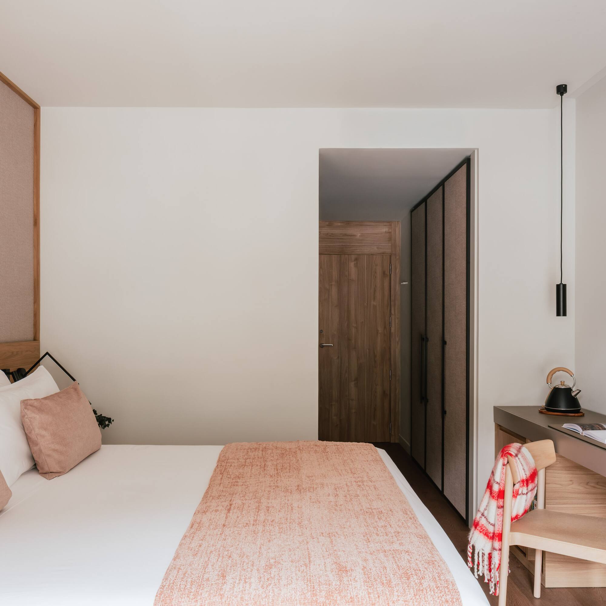 Modern hotel bedroom with cozy bed, wood headboard, desk, and flat-screen TV.