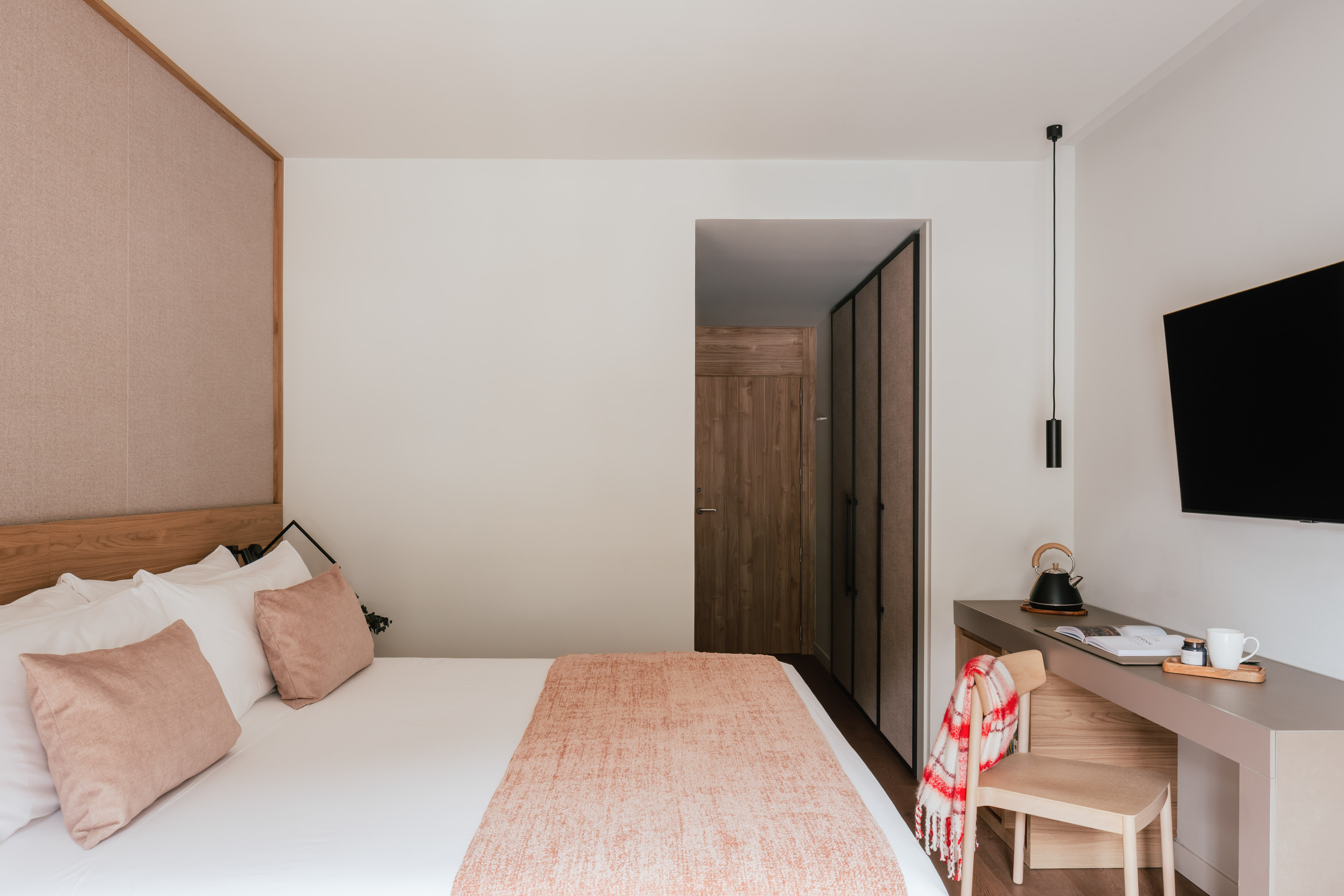 Modern hotel bedroom with cozy bed, wood headboard, desk, and flat-screen TV.