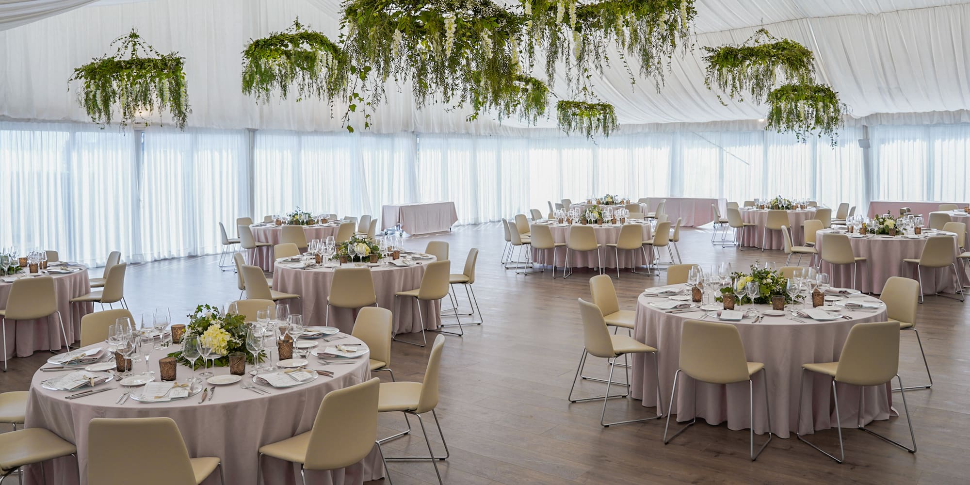 Recepción de boda en carpa, mesas vestidas, sillas claras y follaje colgante.