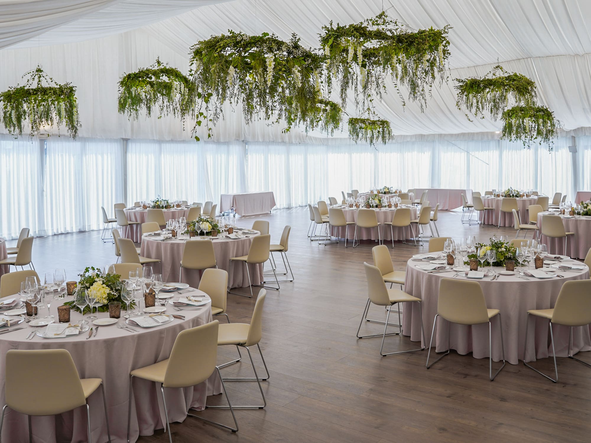Recepción de boda elegante con mesas puestas y decoración floral colgante.