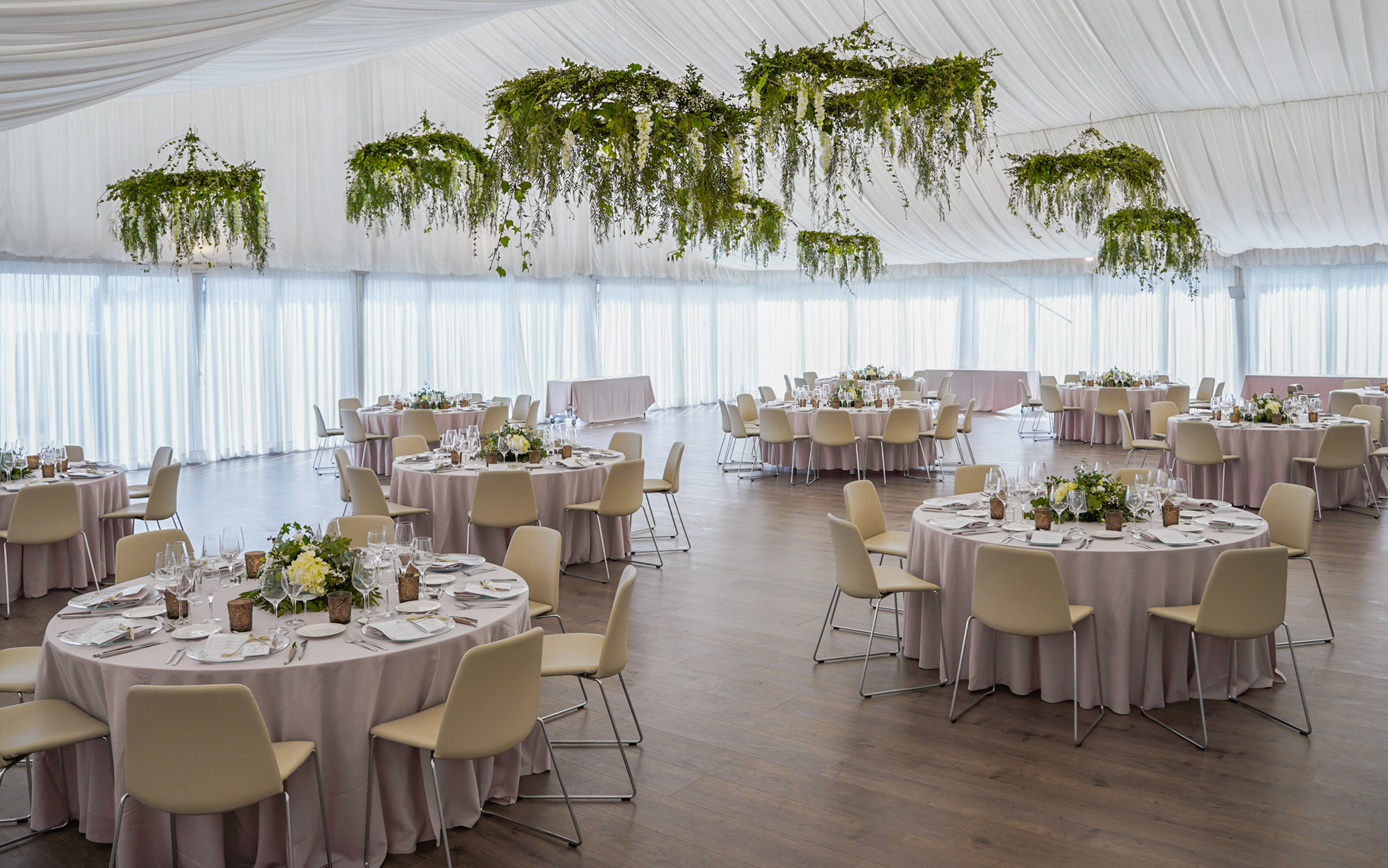 Recepción de boda en carpa, mesas vestidas, sillas claras y follaje colgante.