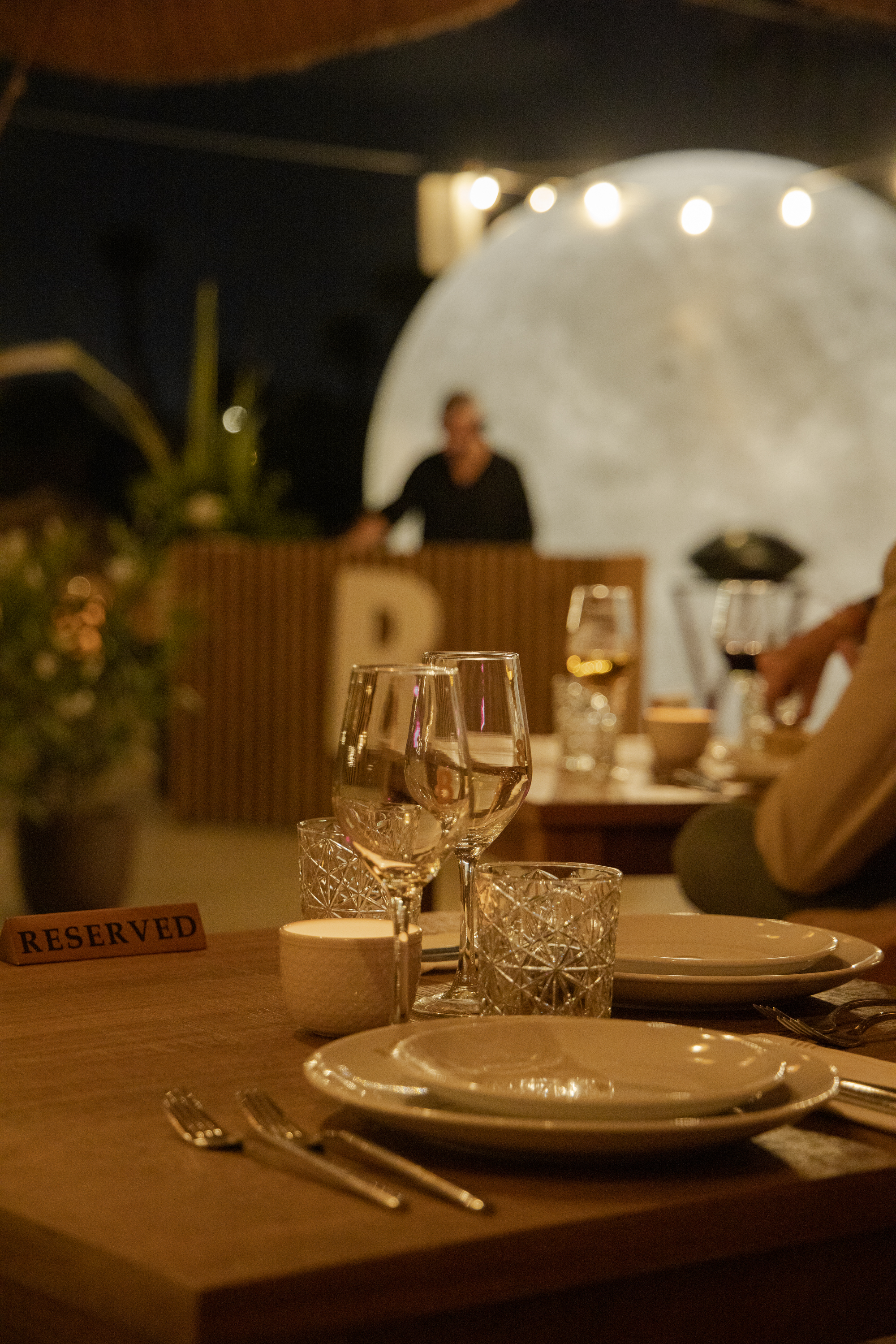 Reserved dining table with wine glasses, plates, and illuminated moon background.