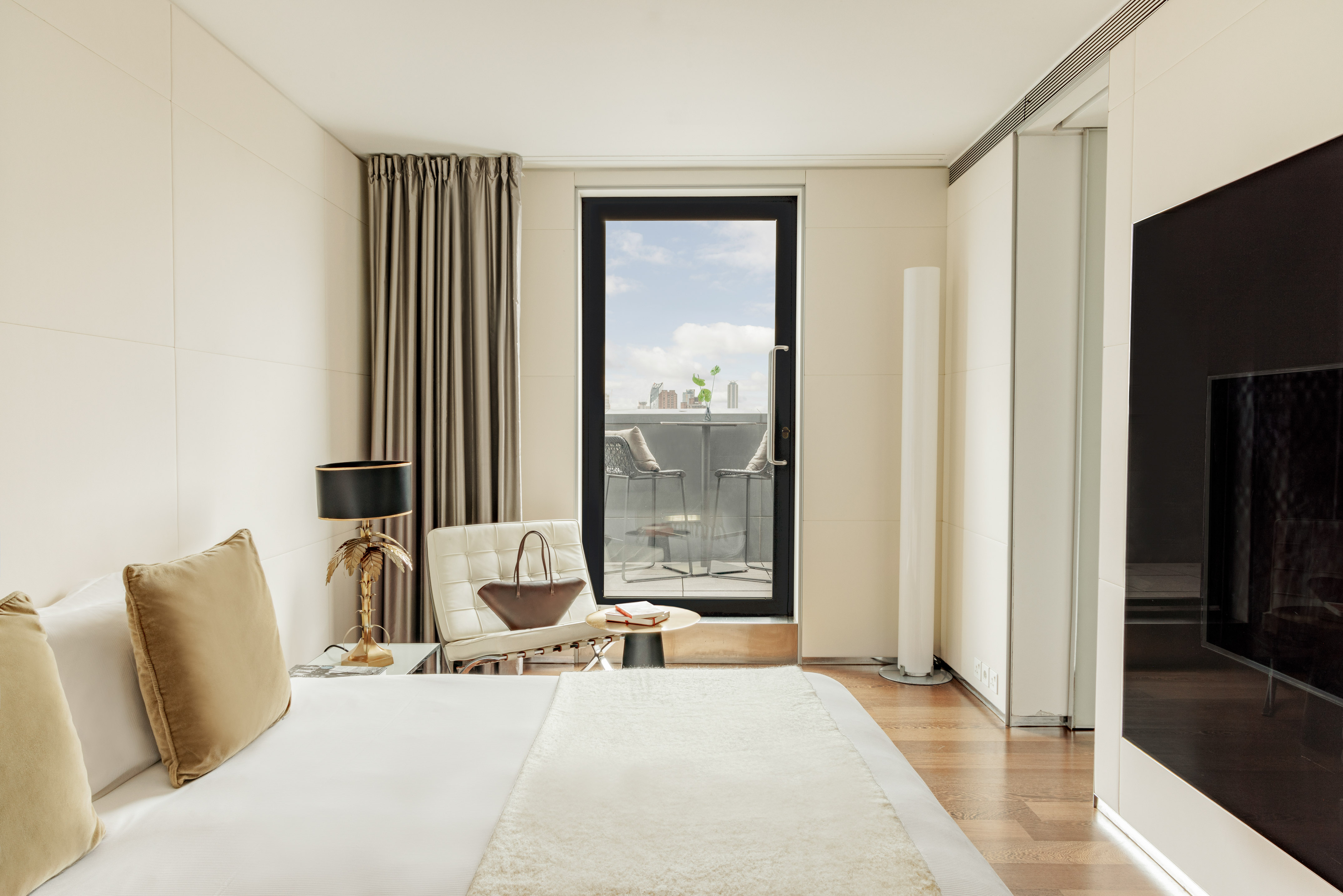 Luxury hotel bedroom with balcony, outdoor seating, large bed, and modern decor.
