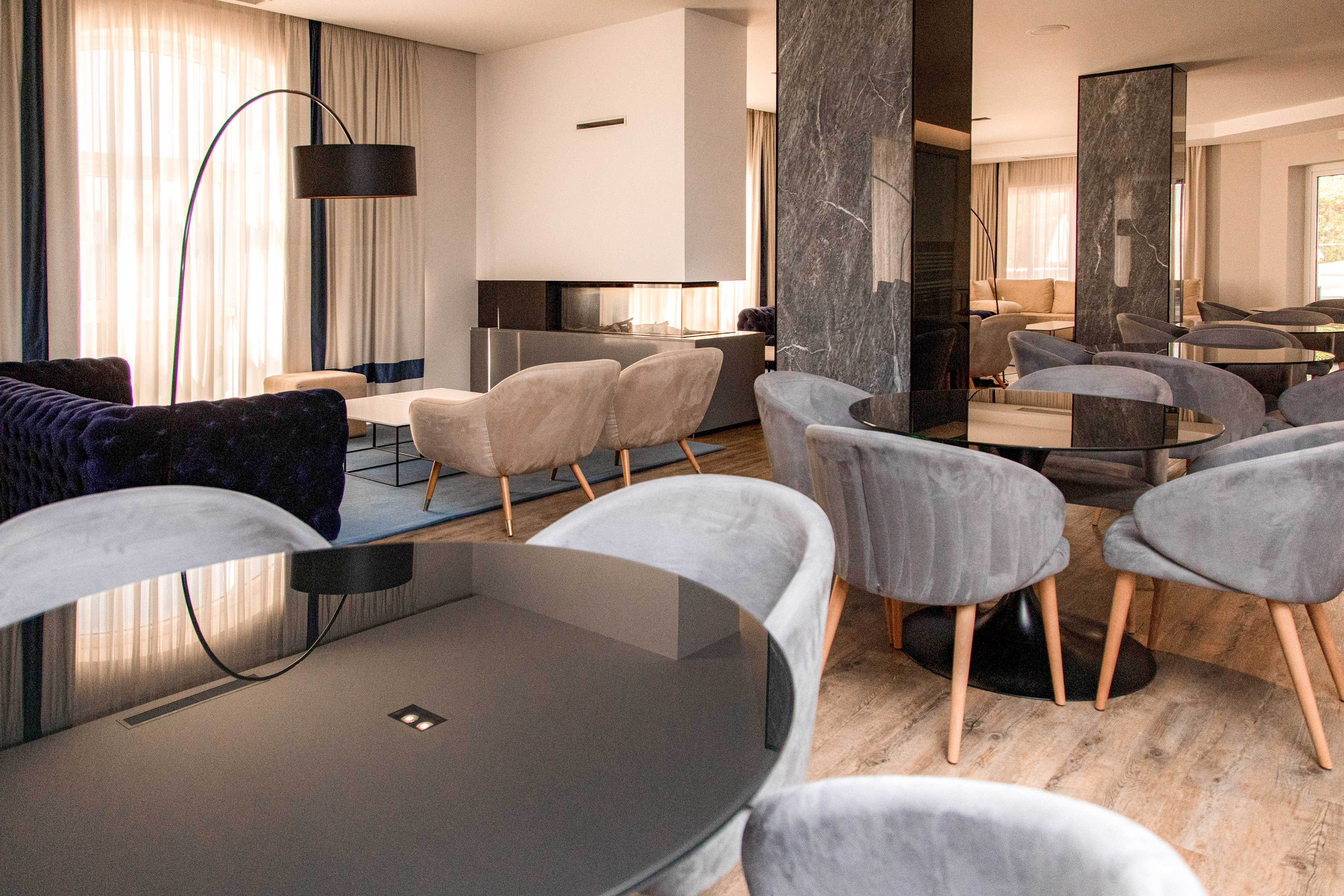 Modern hotel lounge with velvet chairs, glass tables, fireplace, and marble.