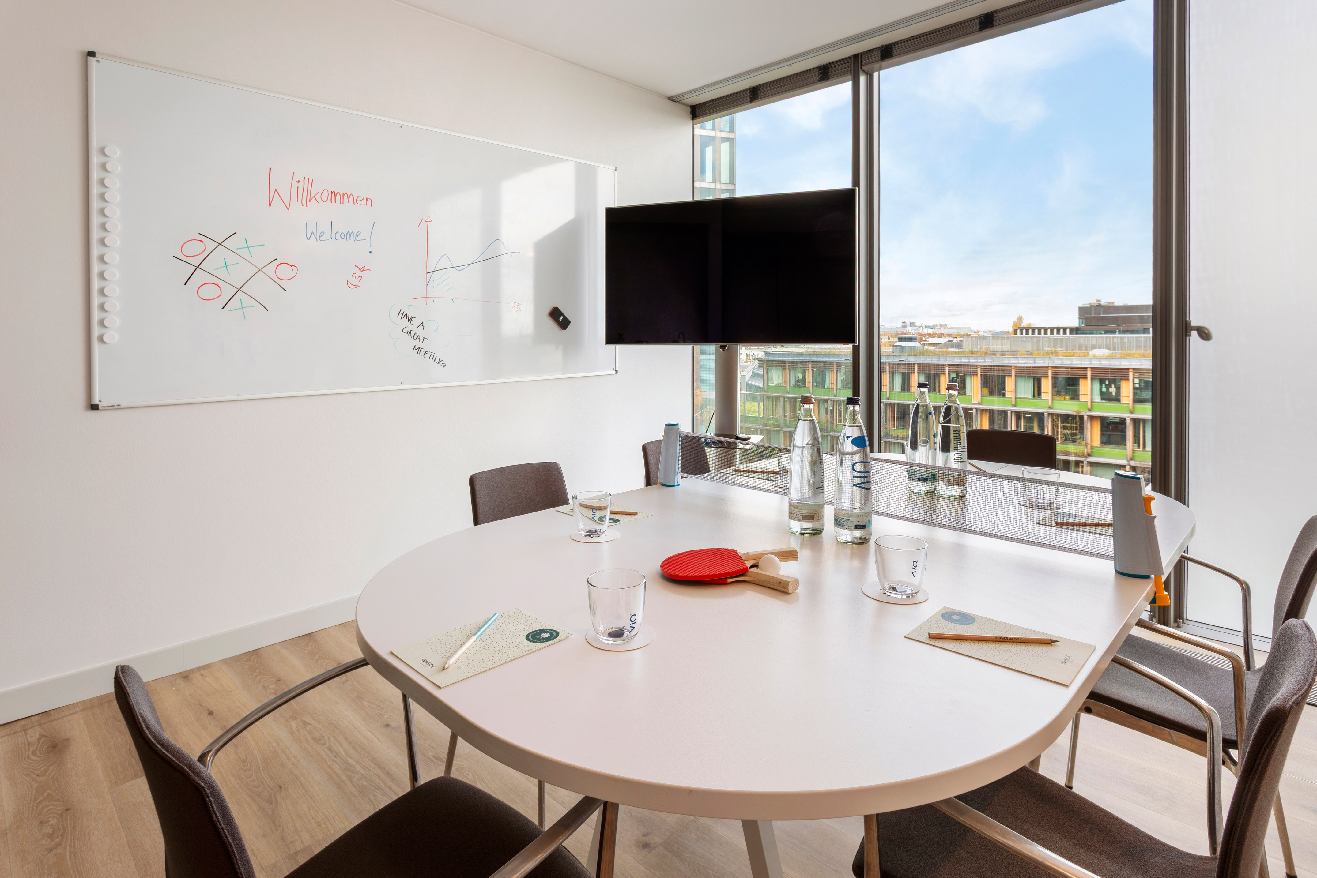 Modern office meeting room with whiteboard, screen, and panoramic city view.