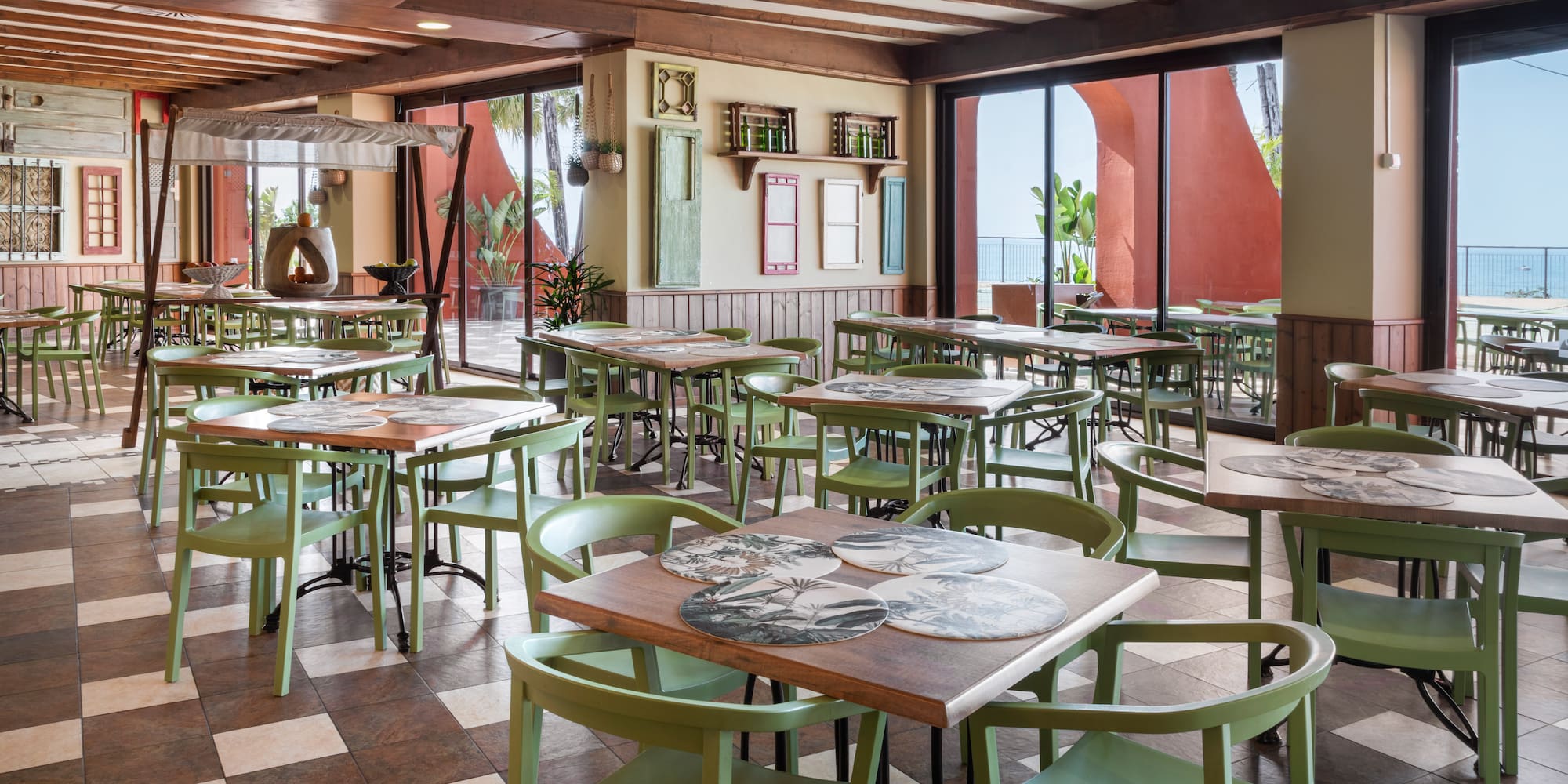 Bright restaurant dining area with green chairs, patterned floor, and sea view.