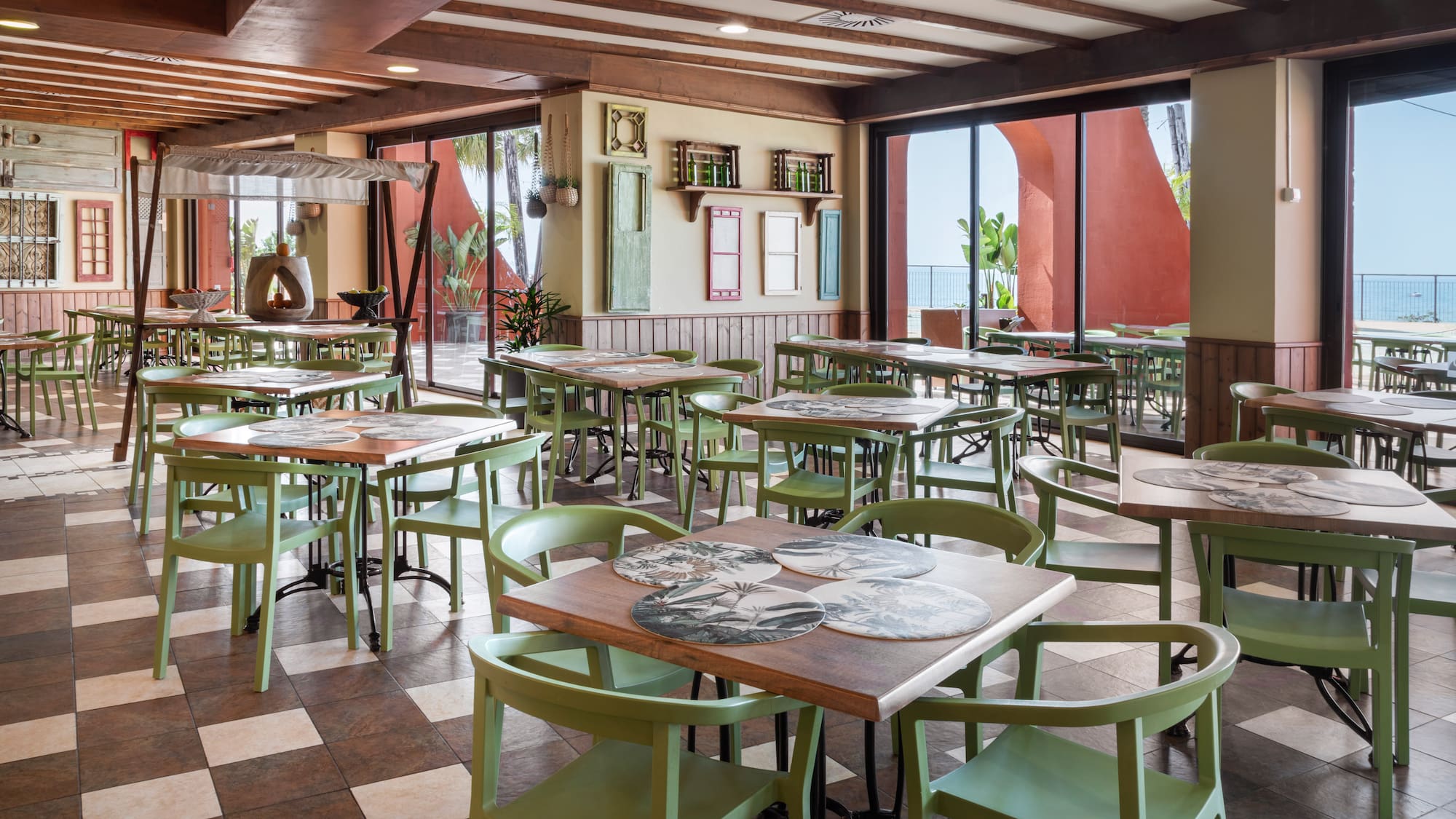 Restaurant dining area with green chairs, wooden tables, and scenic sea views.