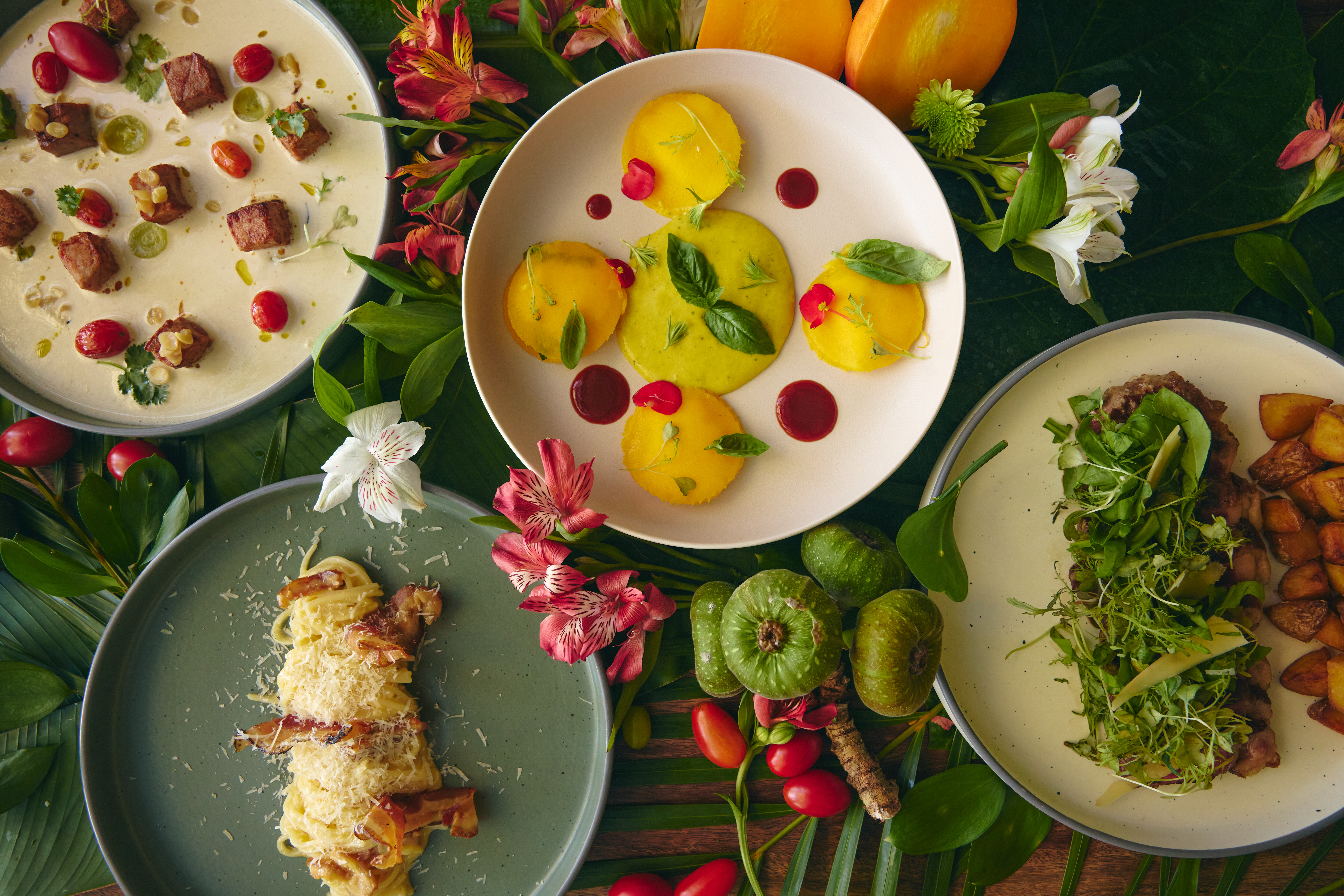 Exquisite gourmet meal presentation: soup, savory polenta, carbonara, steak, tropical setting.