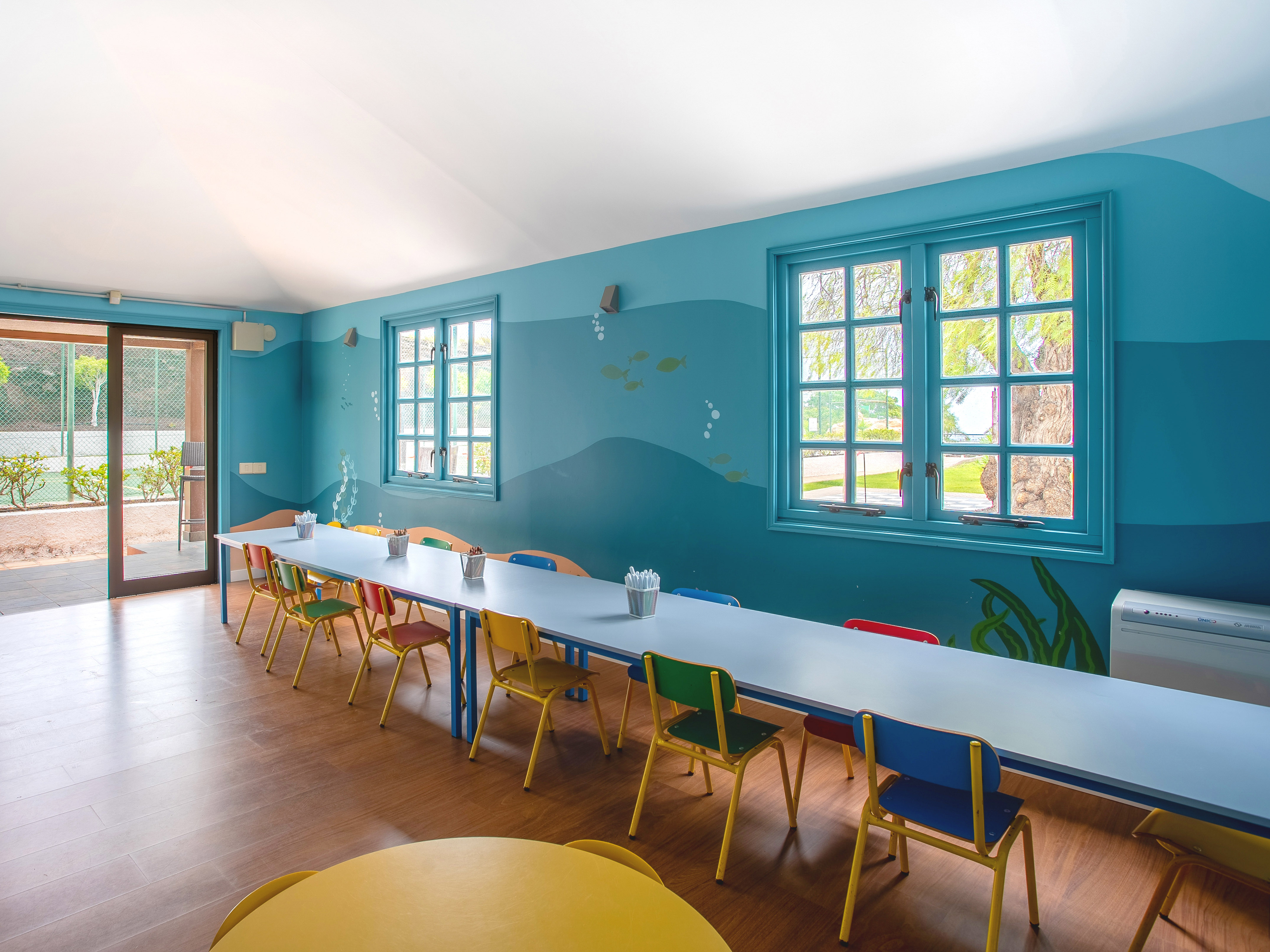 Vibrant kids' playroom with ocean-themed mural, colorful chairs, and activity table.