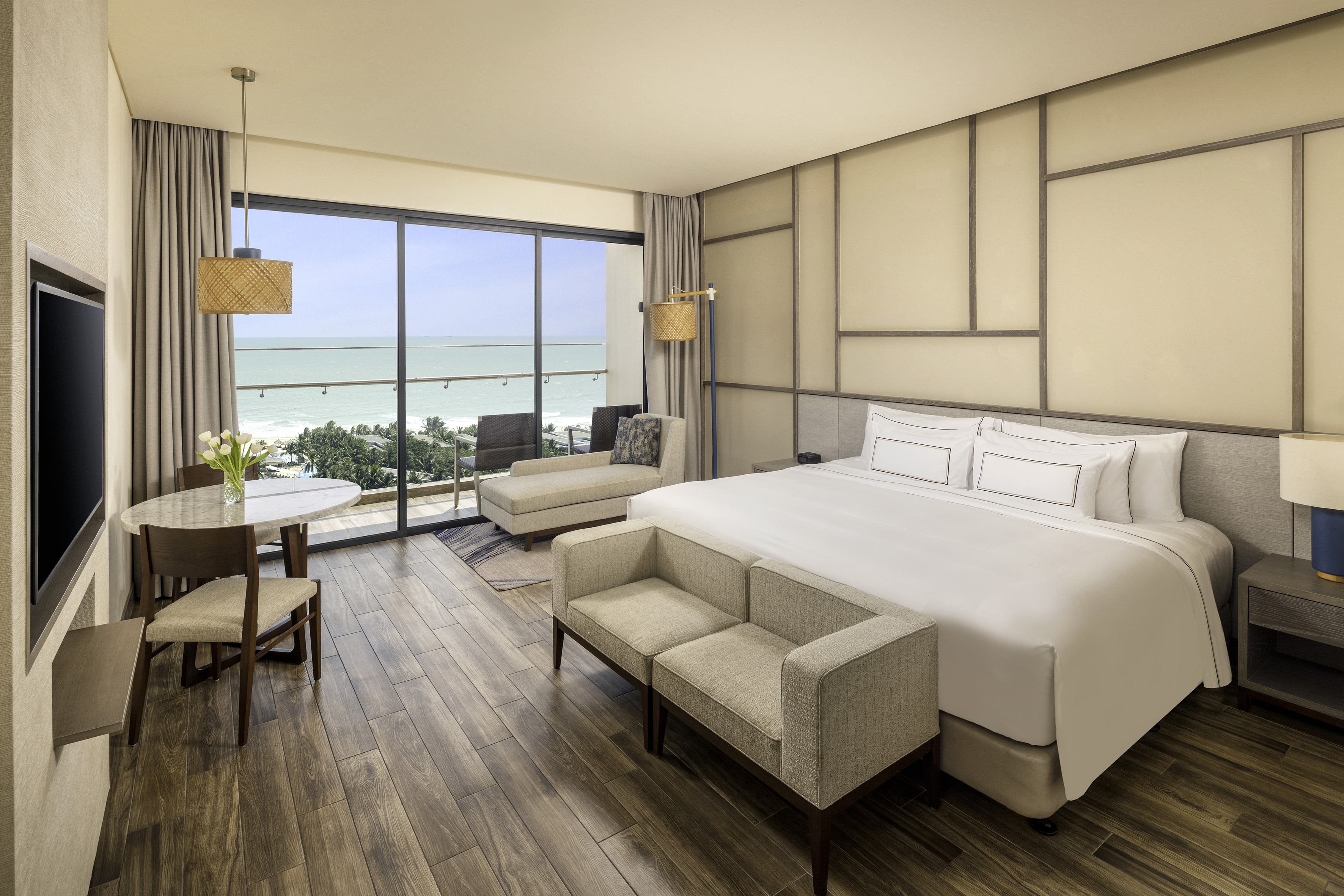 Modern hotel room with ocean view, large bed, dining area, and balcony.