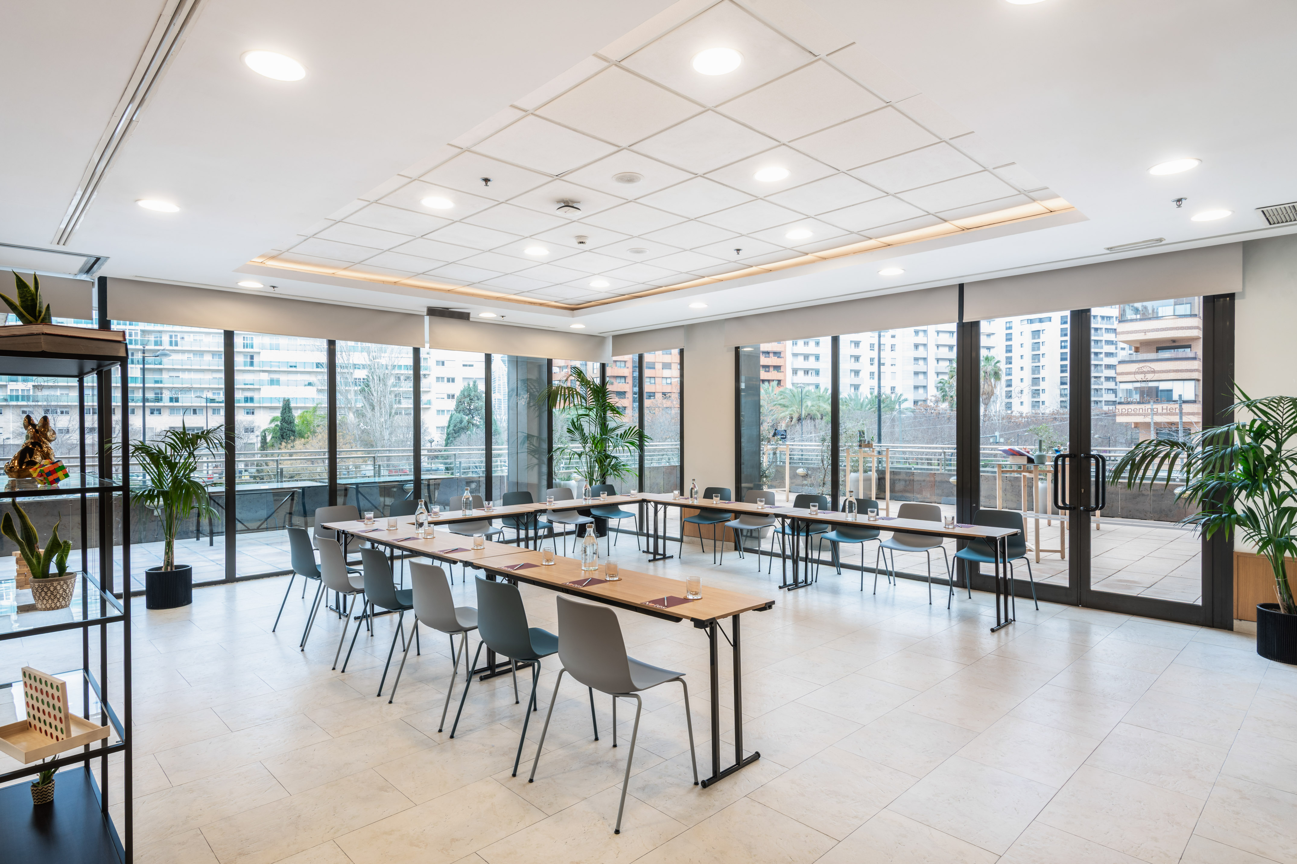 Modern conference room with U-shaped tables, grey chairs, and city views.