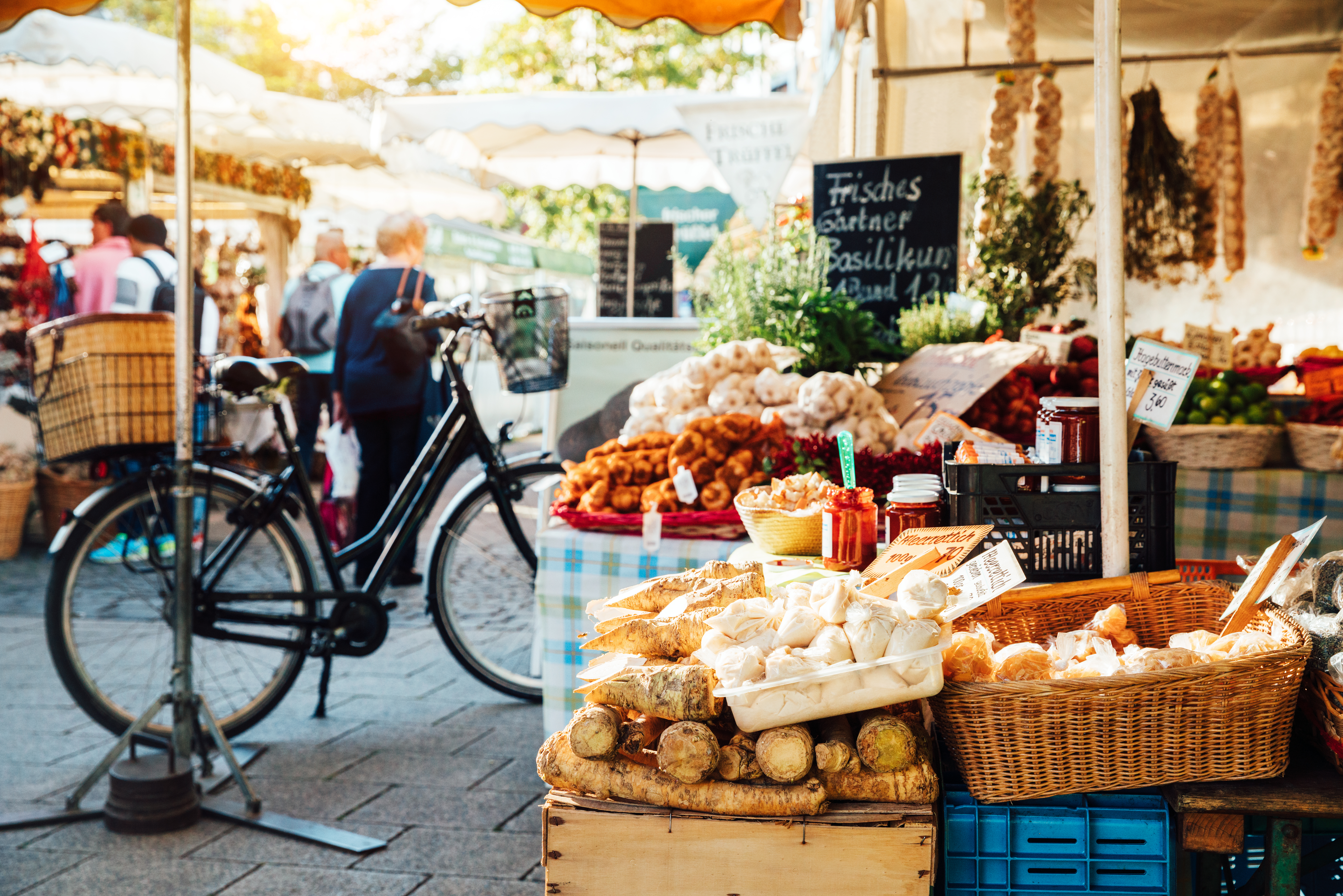 Mercado soleado con puesto de ajo, pan, verduras frescas y bicicleta.