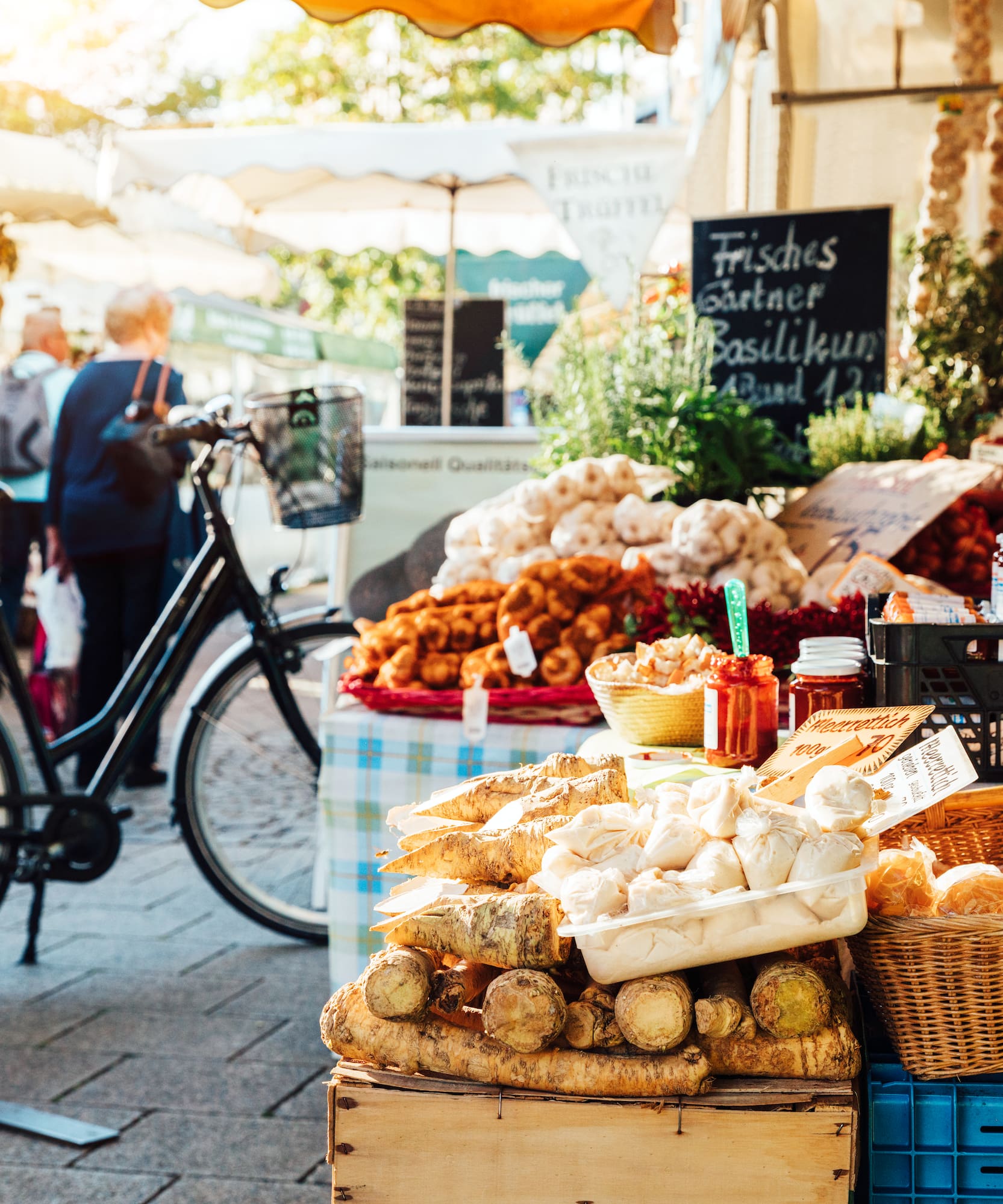 Mercado soleado con puesto de ajo, pan, verduras frescas y bicicleta.