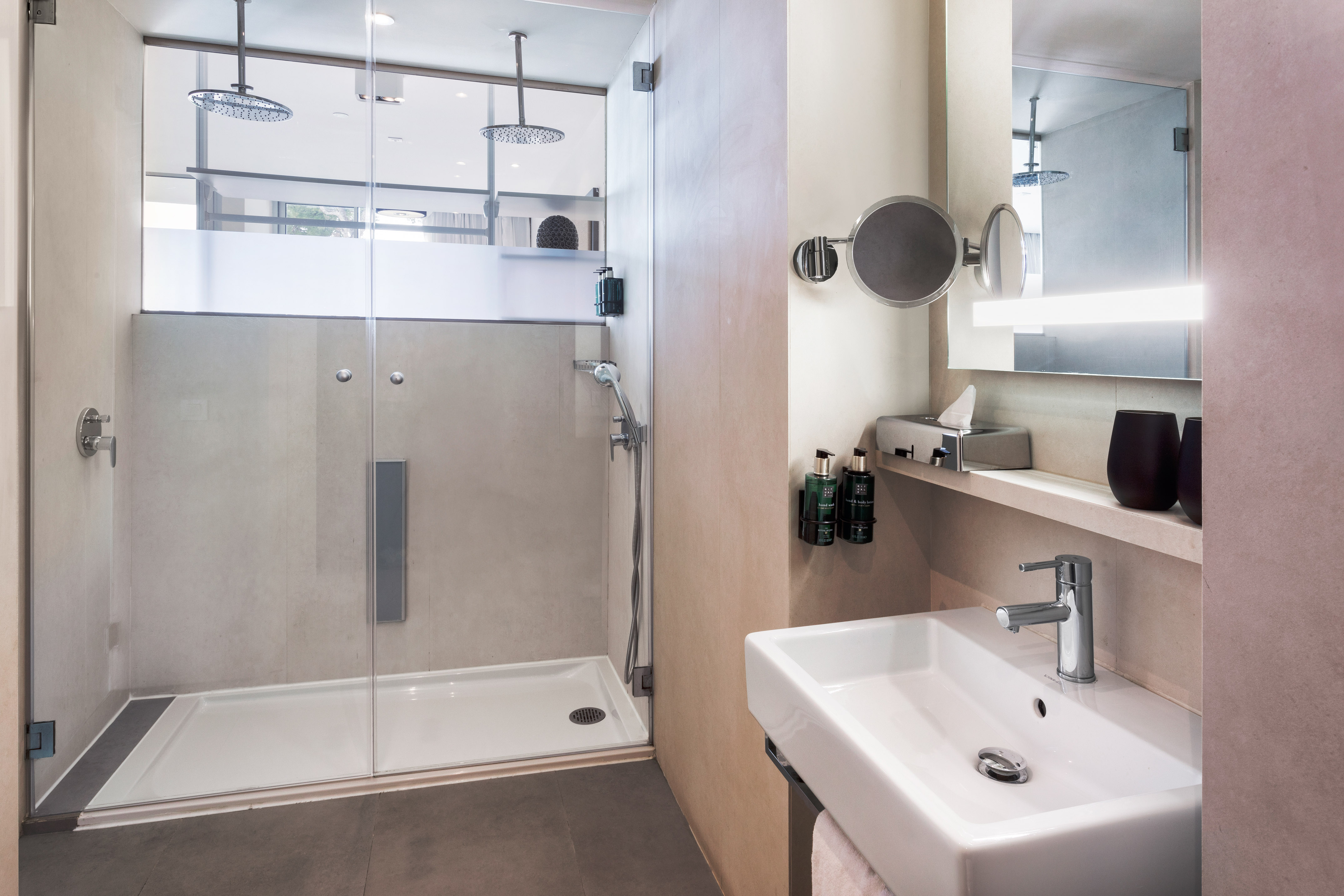Modern hotel bathroom with glass walk-in rain shower, dual heads, and vanity.