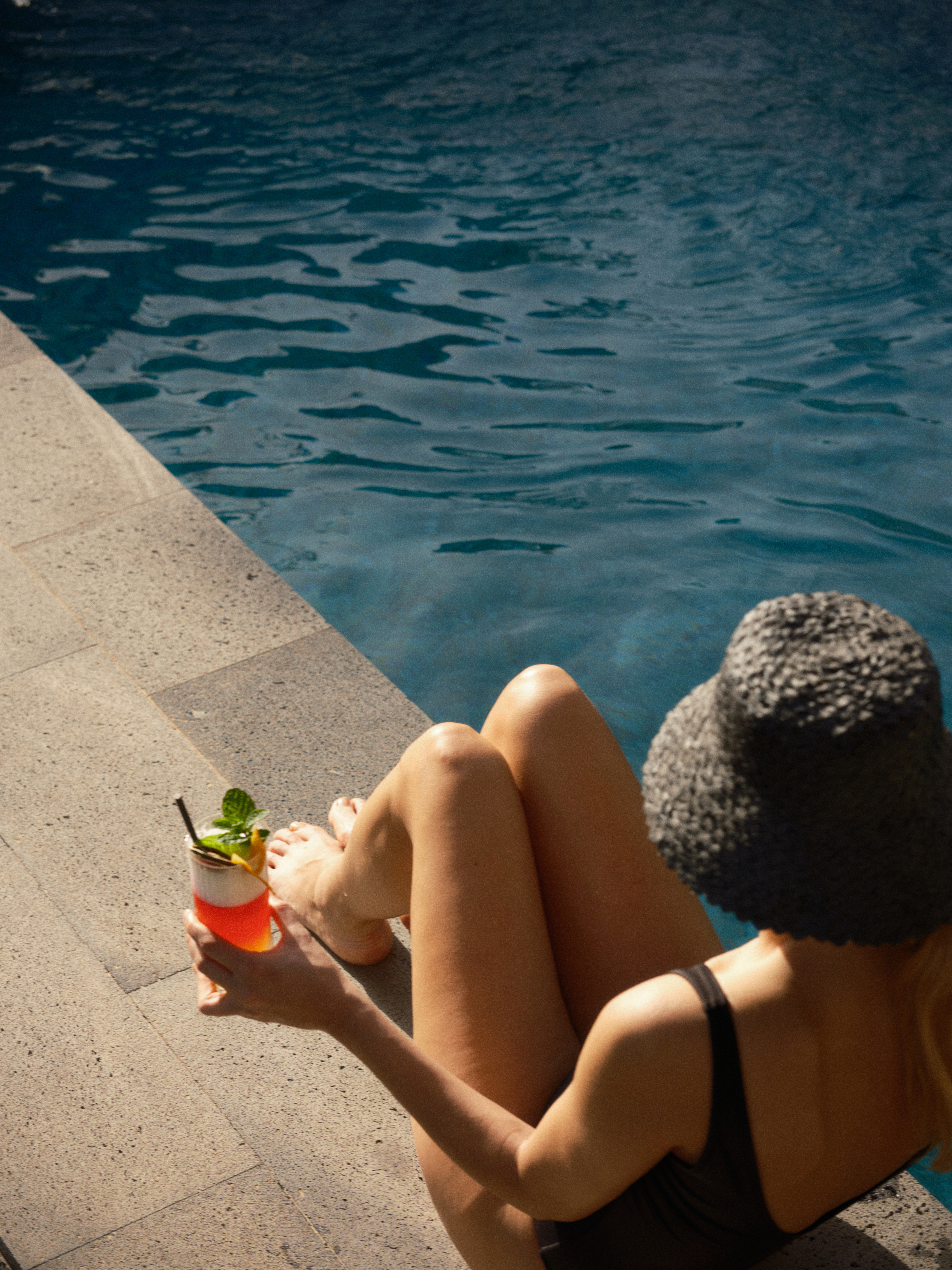 a woman sitting by a pool holding a drink