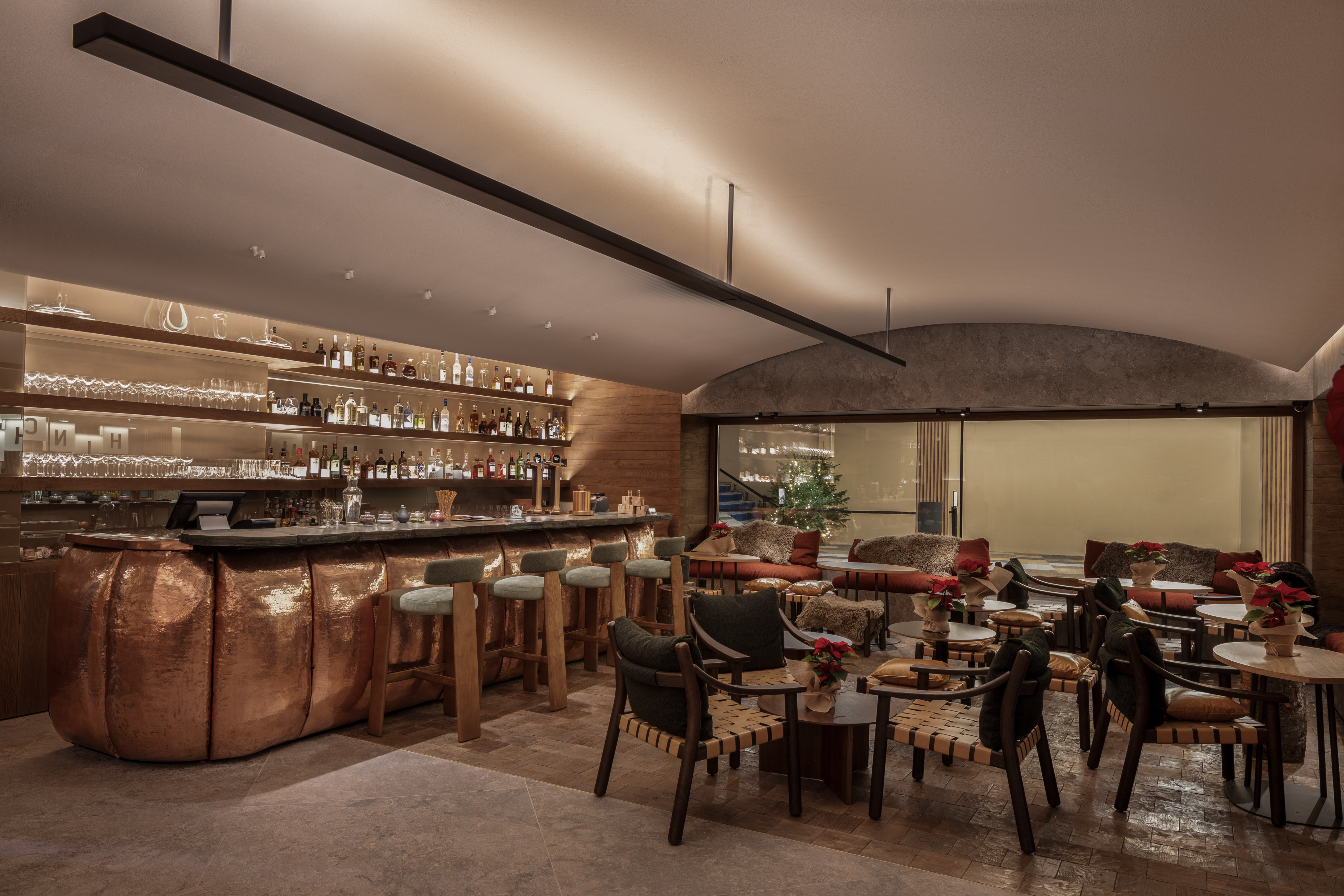 Elegant hotel bar and lounge with copper bar, stylish seating, festive decor.