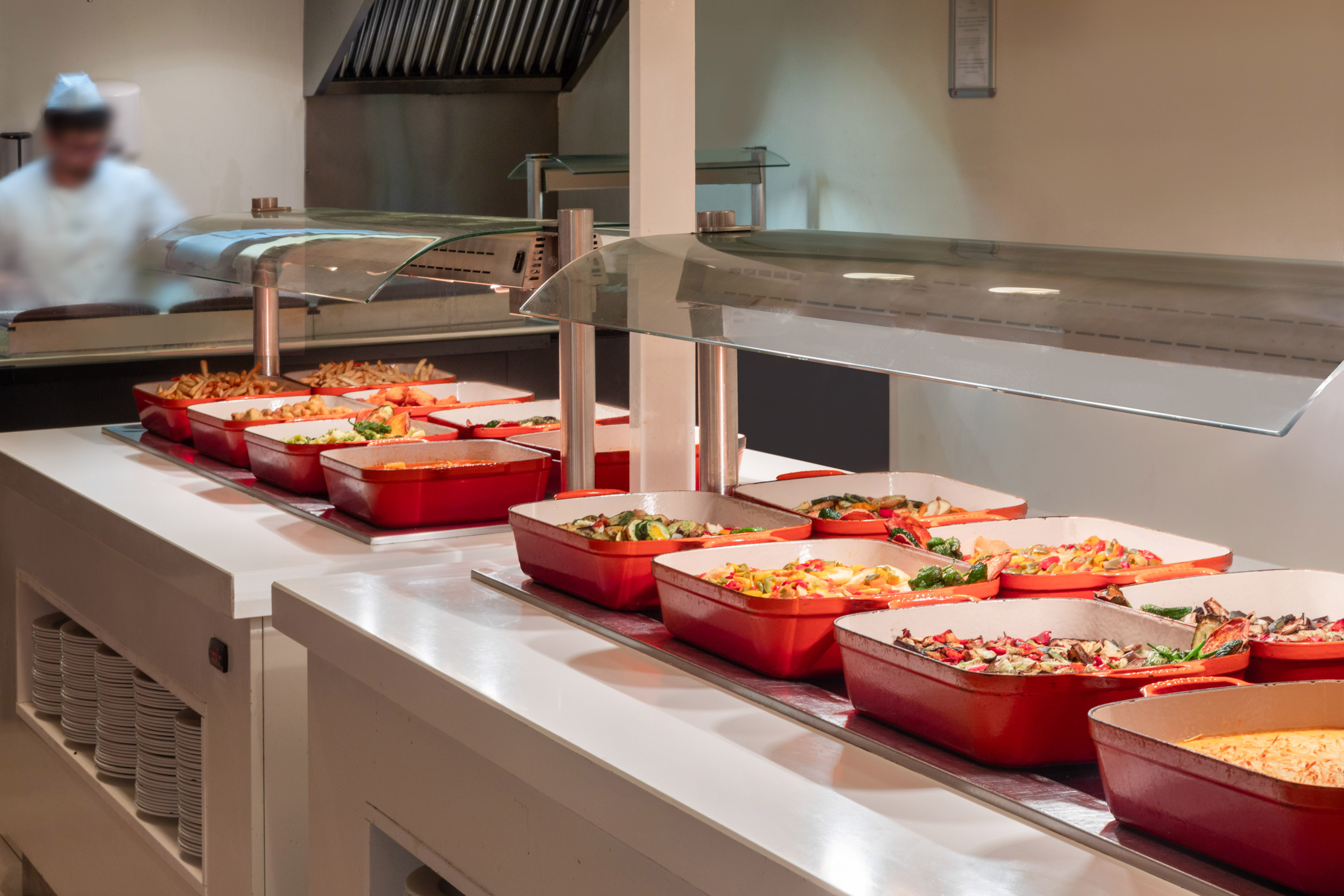 Buffet station with hot dishes in red serving trays and a chef preparing food.