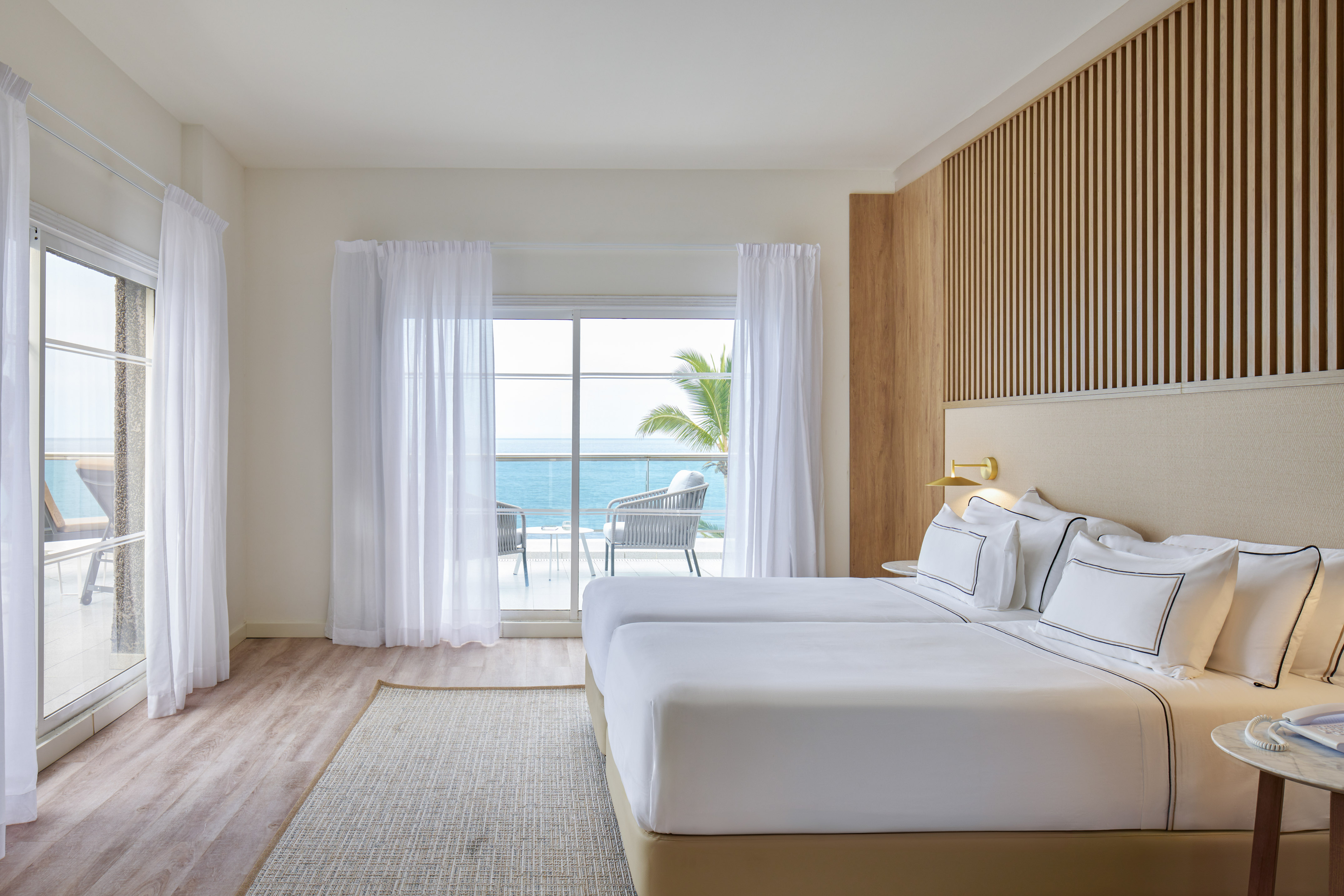 Modern hotel room with twin beds, ocean view balcony, and wood paneling.