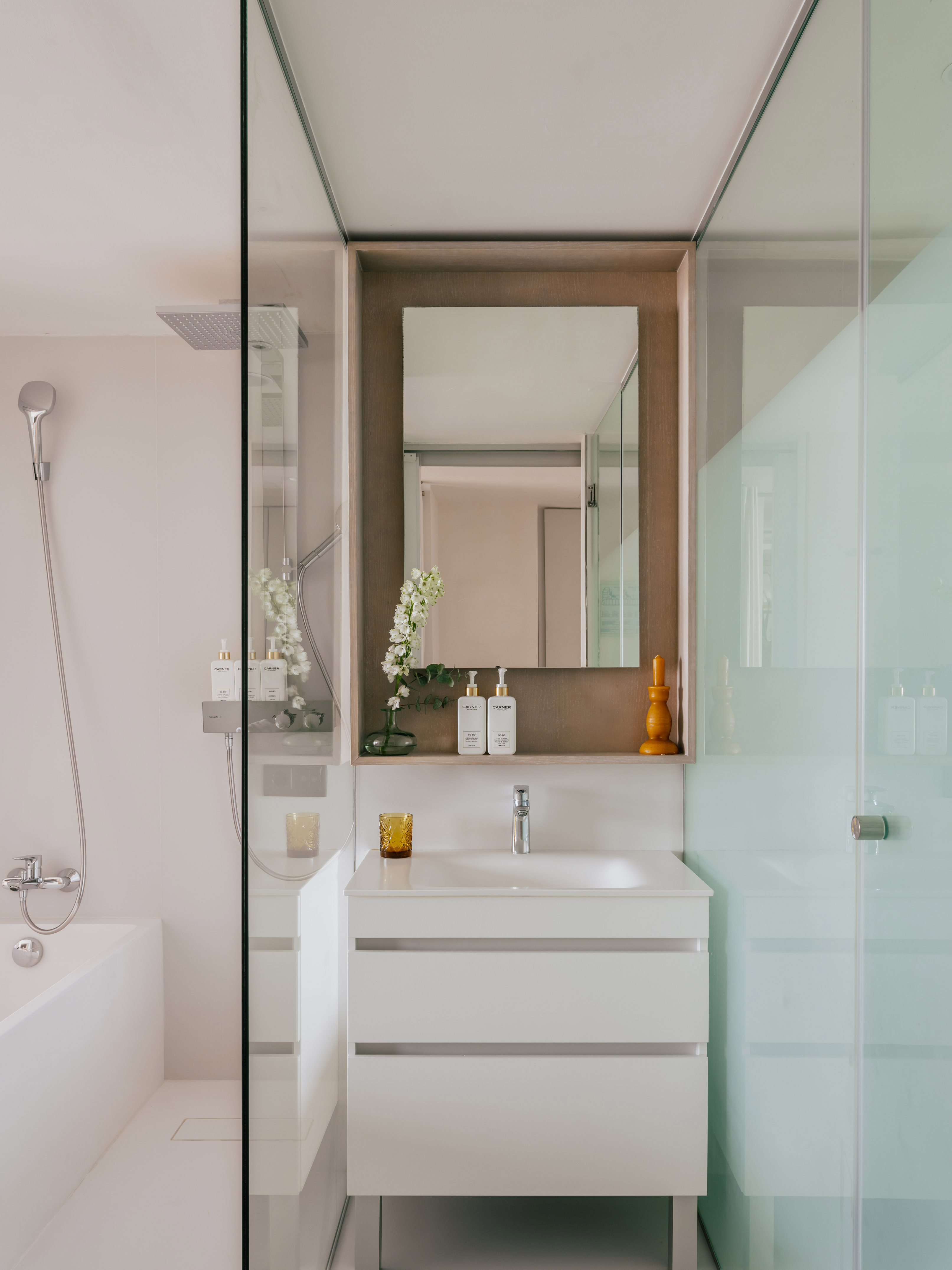 Modern white bathroom with vanity, sink, large mirror, and glass shower enclosure.