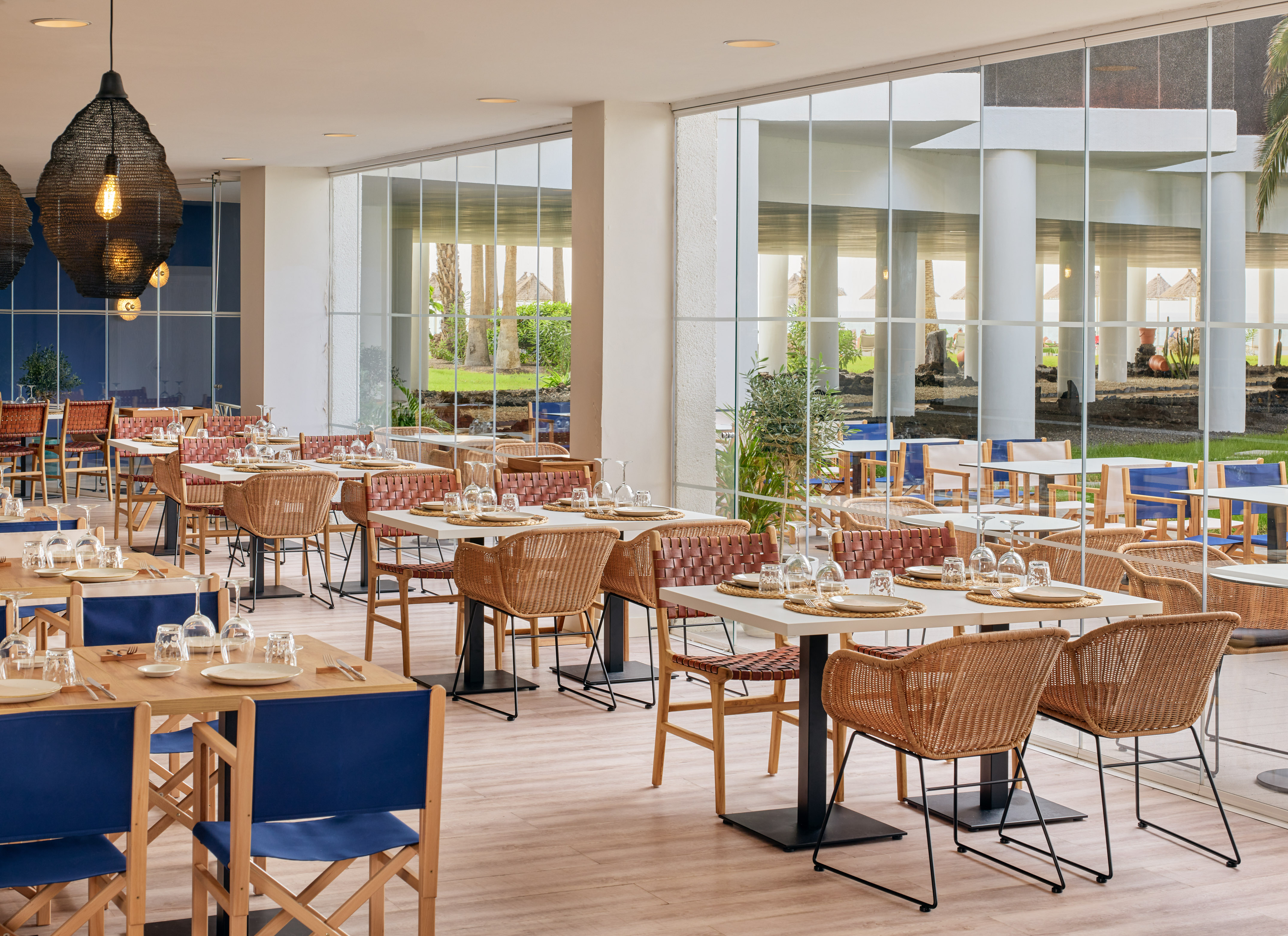 Bright modern restaurant with wicker chairs, set tables, and large windows.