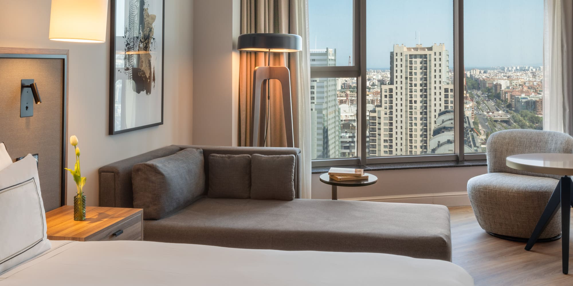 Suite de hotel moderna con sofá, cama y vista panorámica de la ciudad.