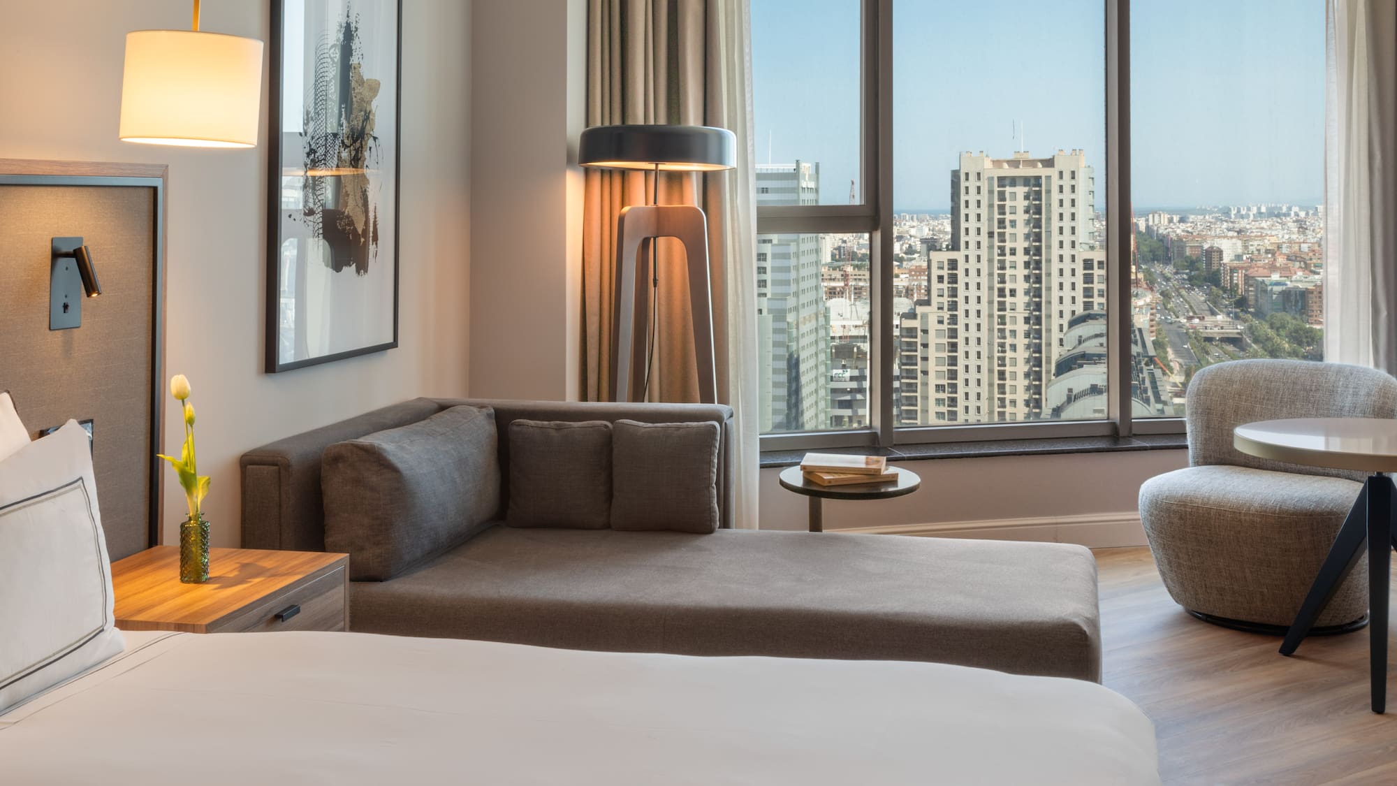 Suite de hotel moderna con sofá, cama y vista panorámica de la ciudad.