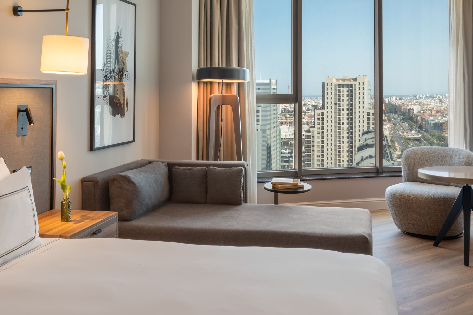 Suite de hotel moderna con sofá, cama y vista panorámica de la ciudad.