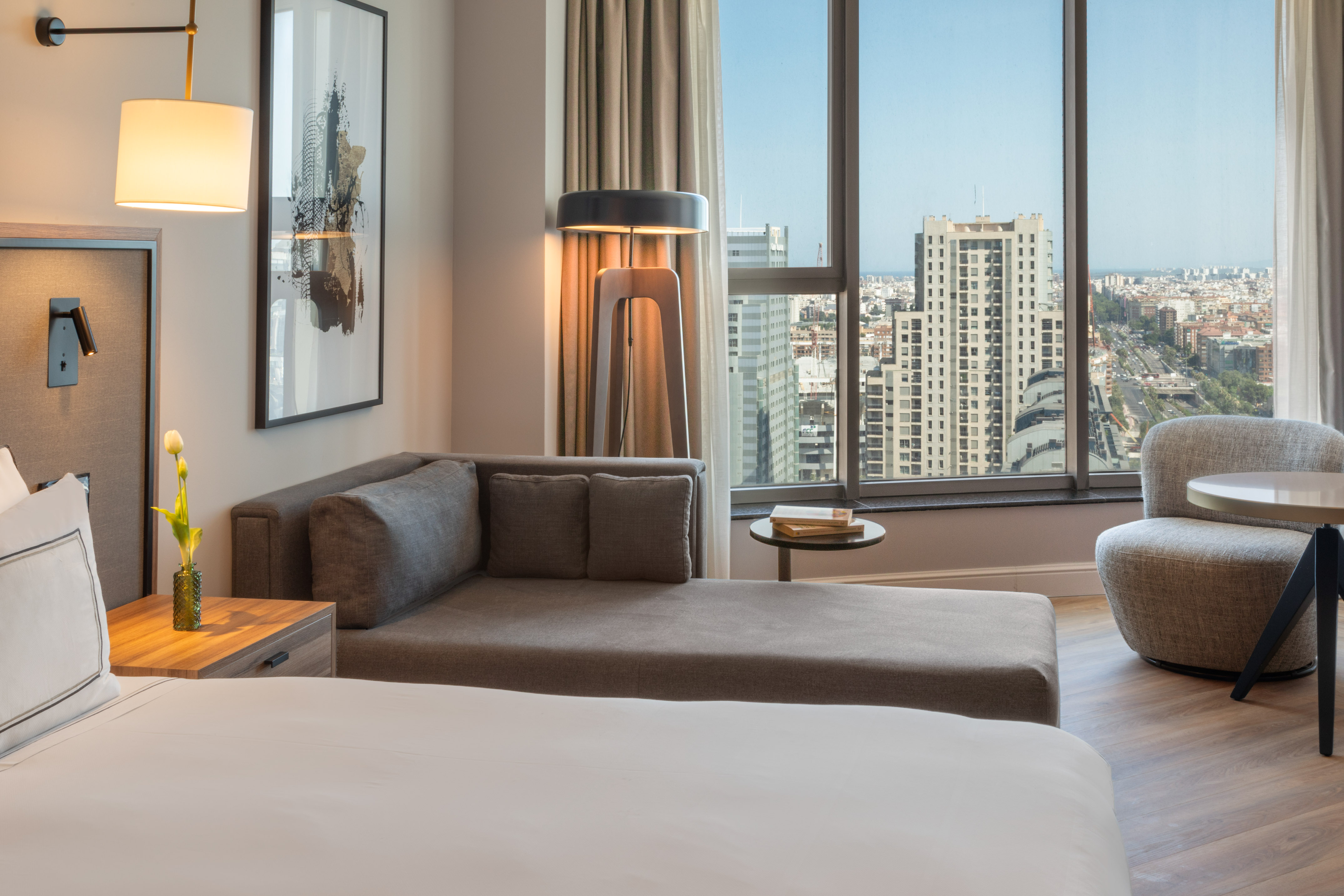 Suite de hotel moderna con sofá, cama y vista panorámica de la ciudad.
