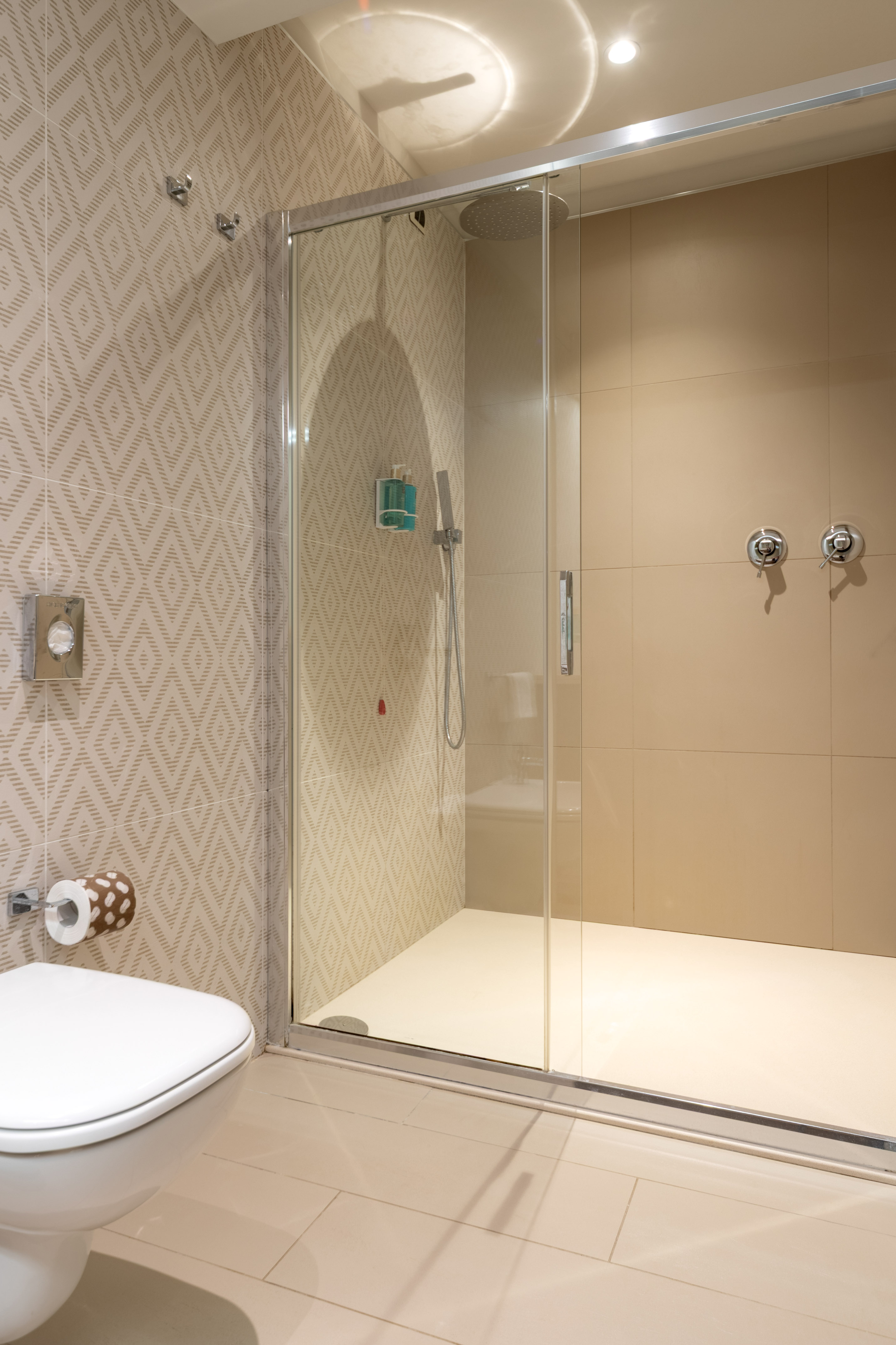 Beige tiled modern bathroom with glass walk-in shower and white toilet.