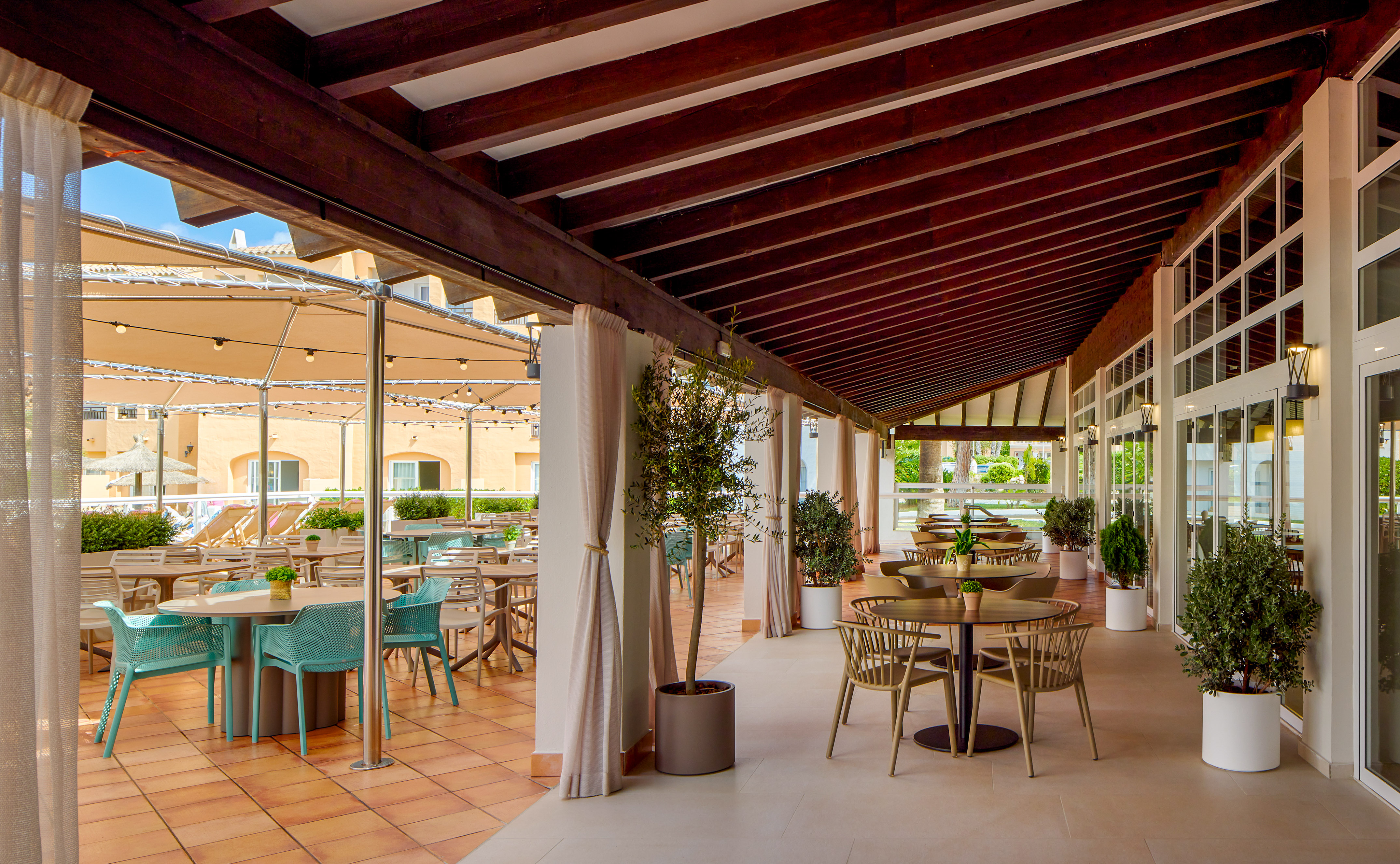 Hotel terrace restaurant with covered outdoor seating and potted plants.