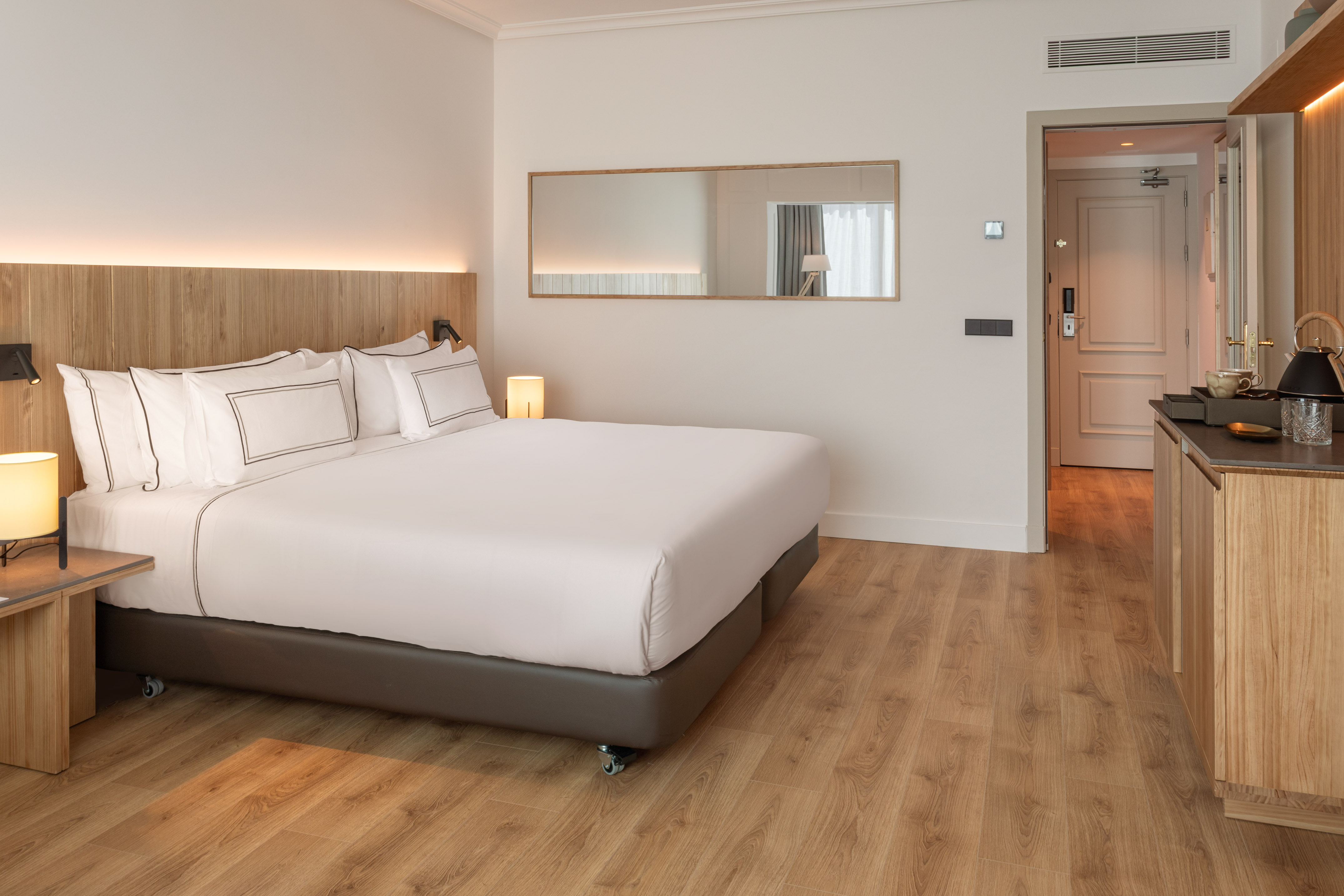 Modern hotel room with king bed, wooden floor, and stylish mirror.