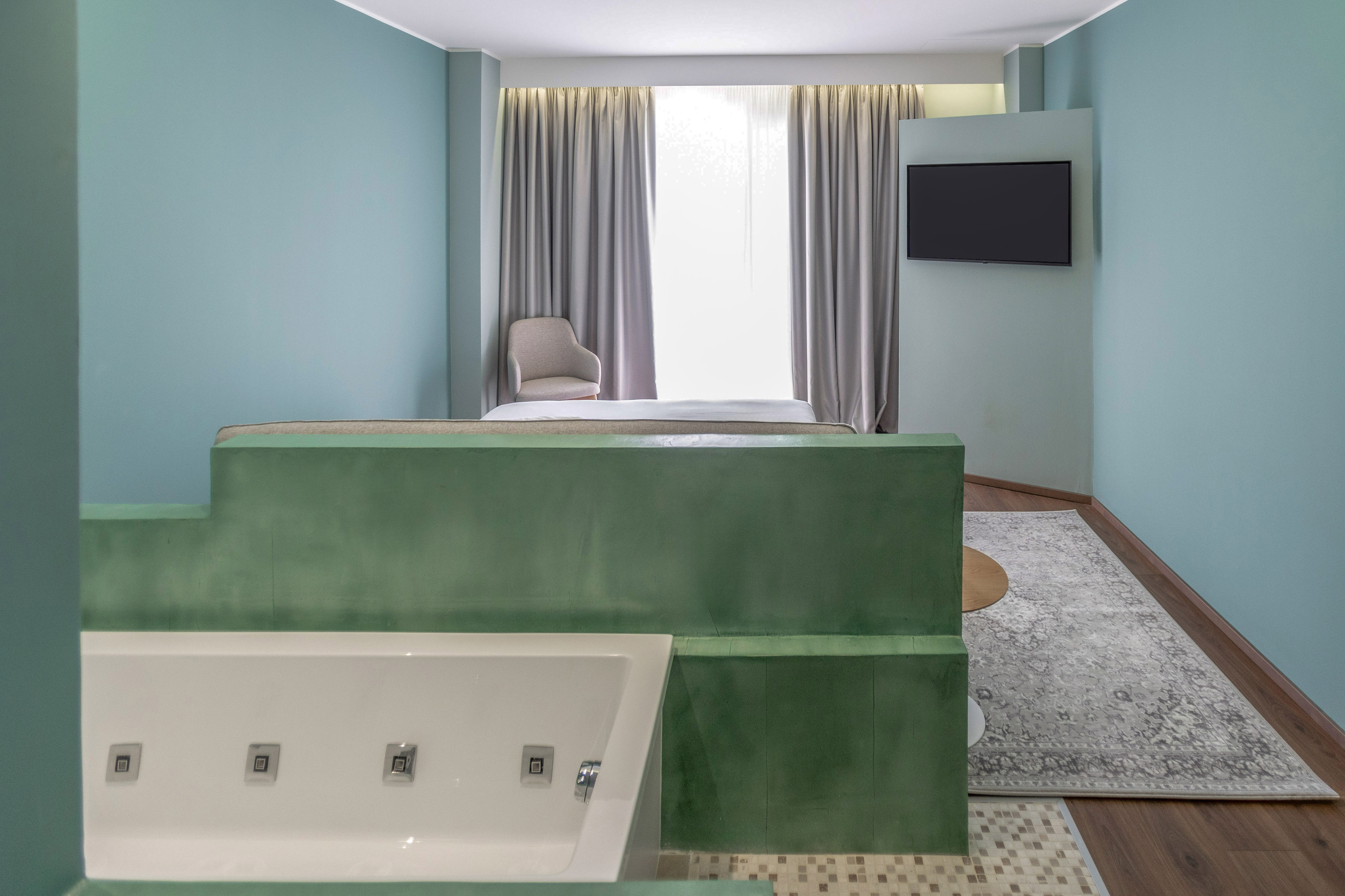 Modern hotel room with integrated white jacuzzi, green partition, bed, and blue walls.
