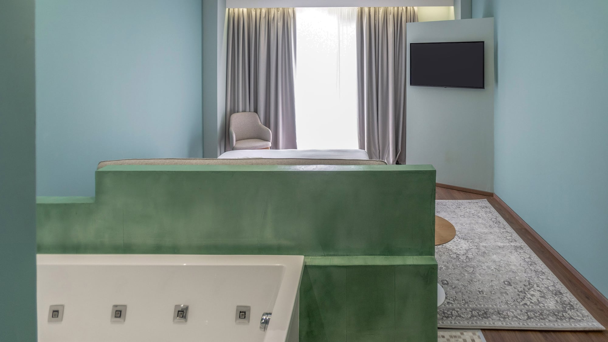 Modern hotel room with integrated white jacuzzi, green partition, bed, and blue walls.