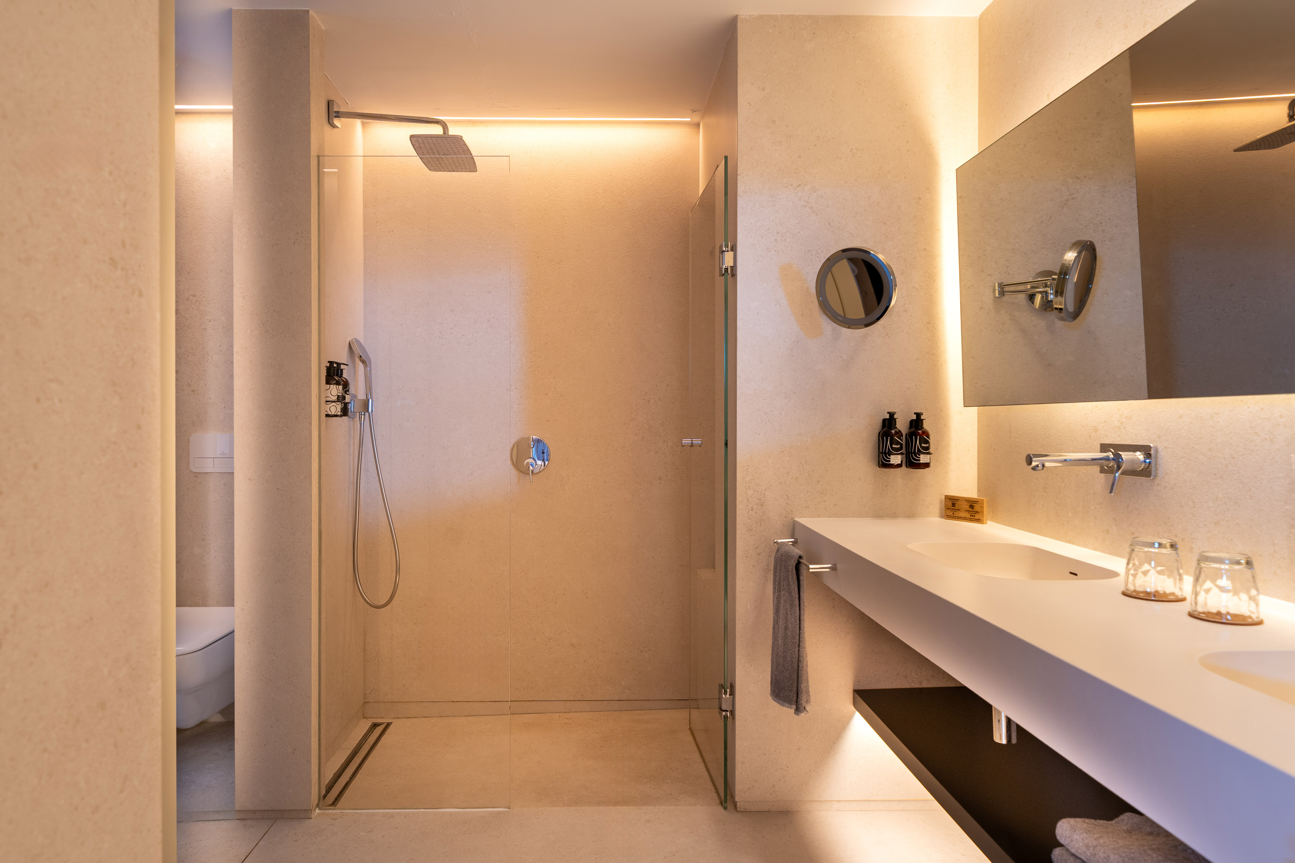 Modern bathroom with walk-in shower, stone walls, vanity, mirror, accent lighting.
