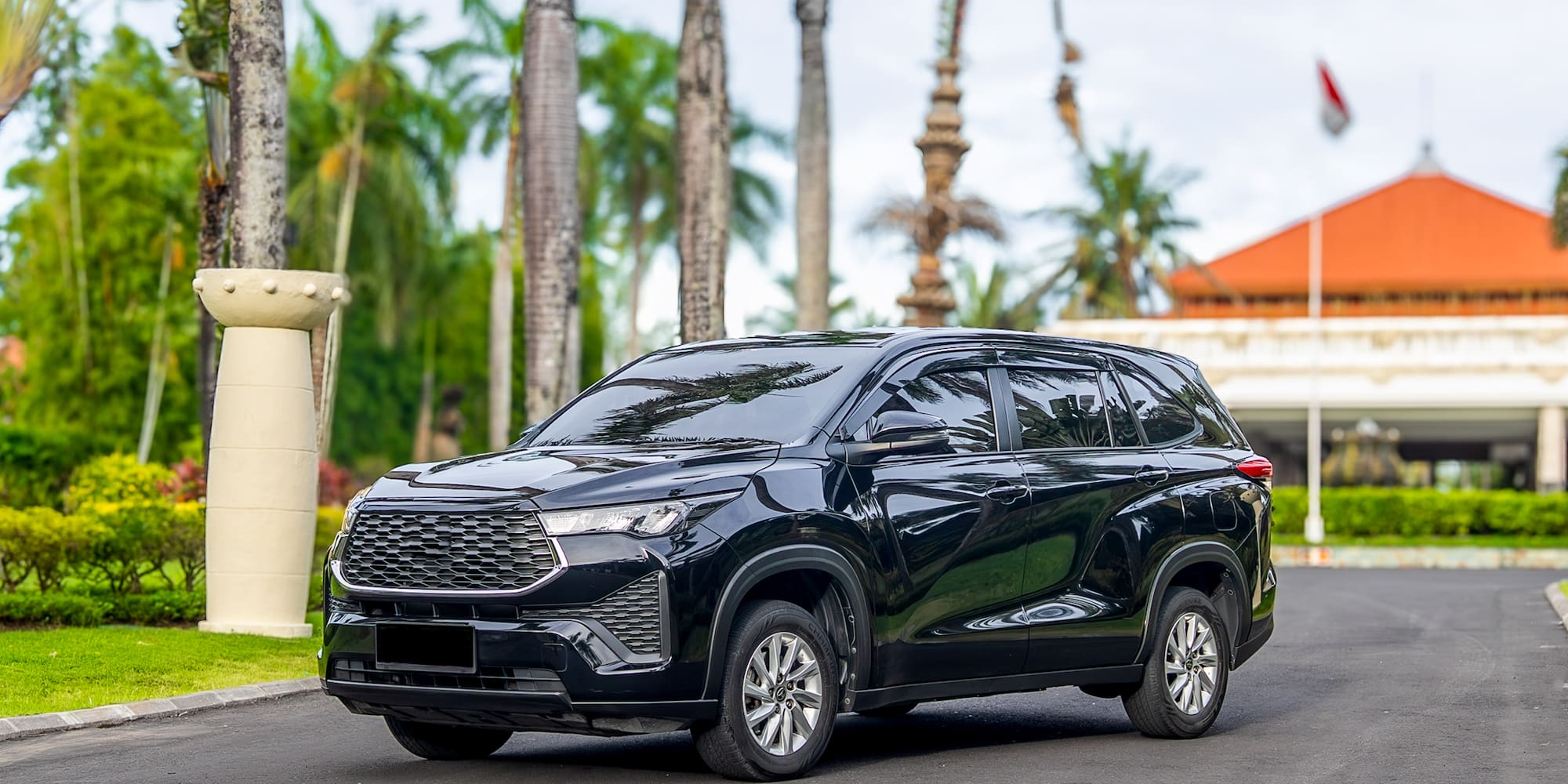 Black modern SUV on a tropical resort driveway with palm trees.